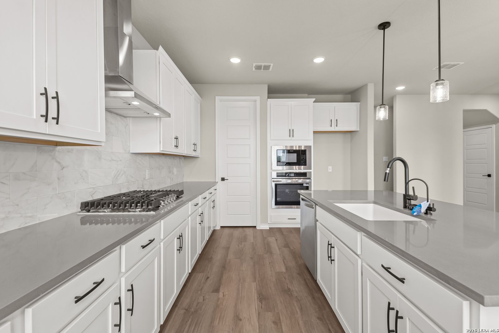 Modern kitchen with white cabinets, quartz countertops, and stainless steel appliances in The Danbury H, Castroville, TX.