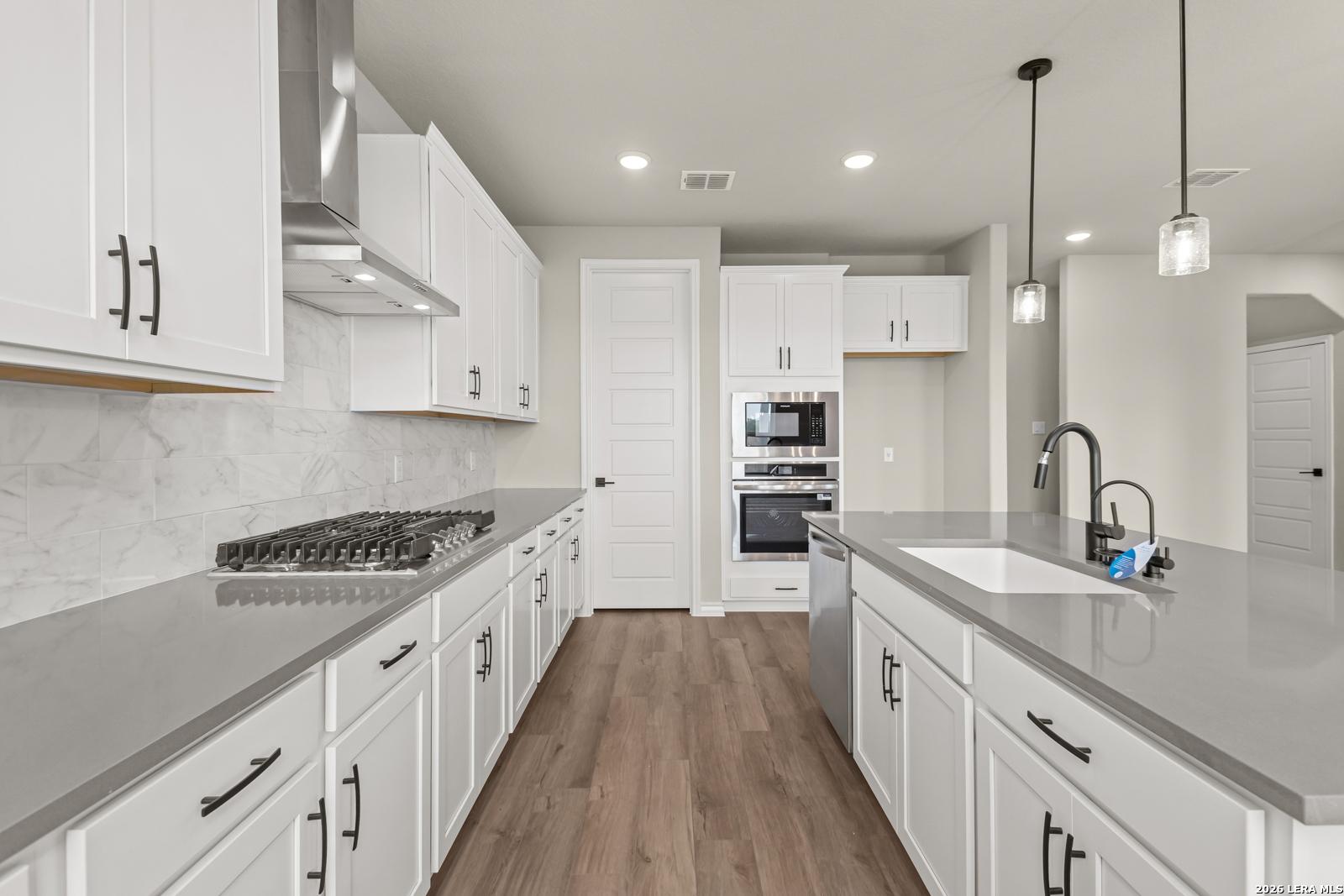 Modern kitchen with white cabinets, quartz countertops, and stainless steel appliances in The Danbury H, Castroville, TX.