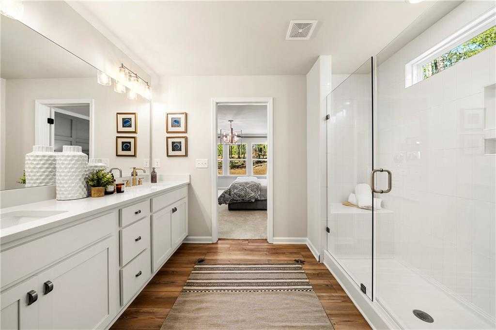 Elegant master bathroom with double white vanity, frameless glass shower, and bedroom view in Davidson Homes Hickory B, Dallas, Georgia