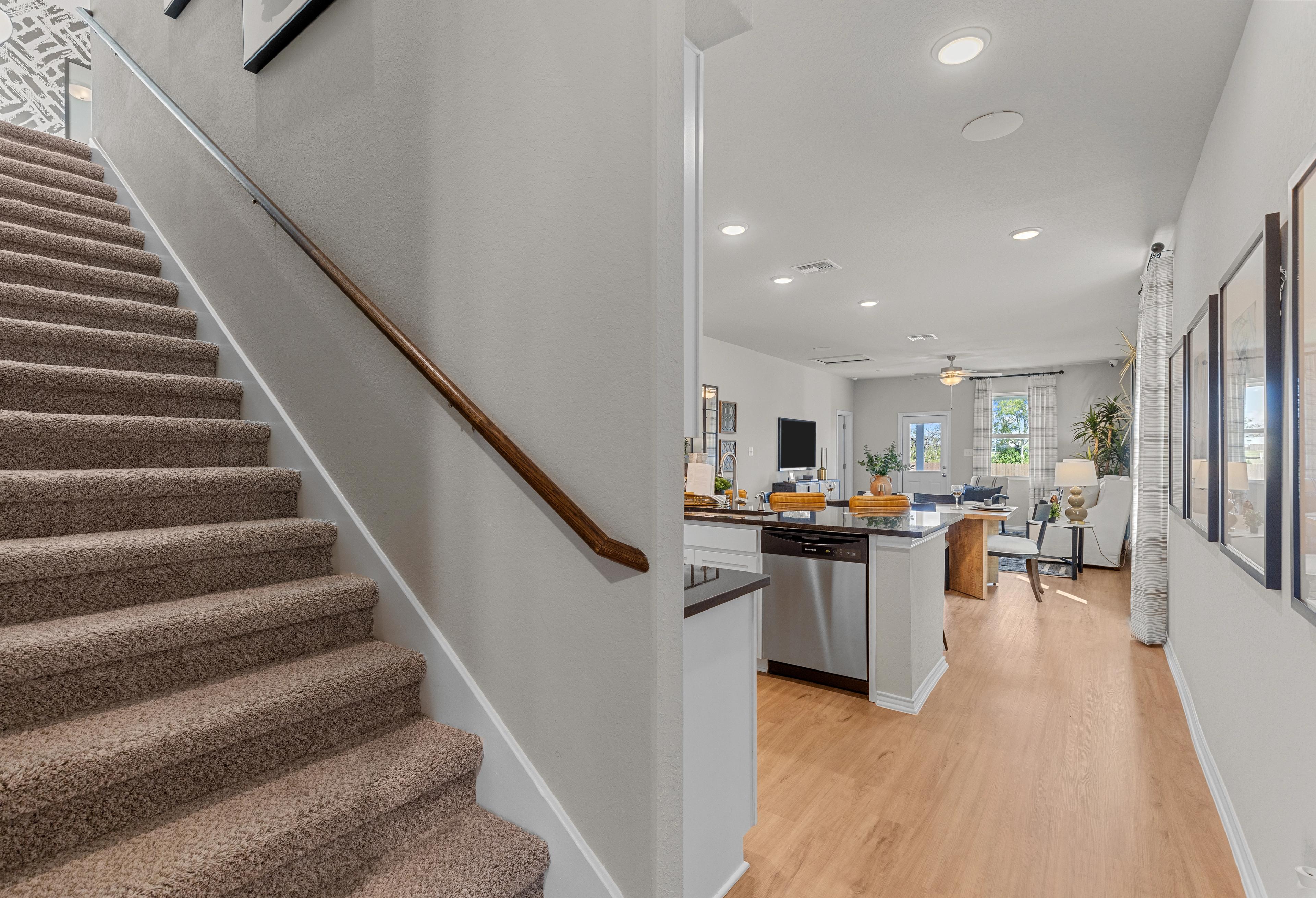 Open kitchen with island and living area adjacent to carpeted staircase in The Sabine A 2-story home design