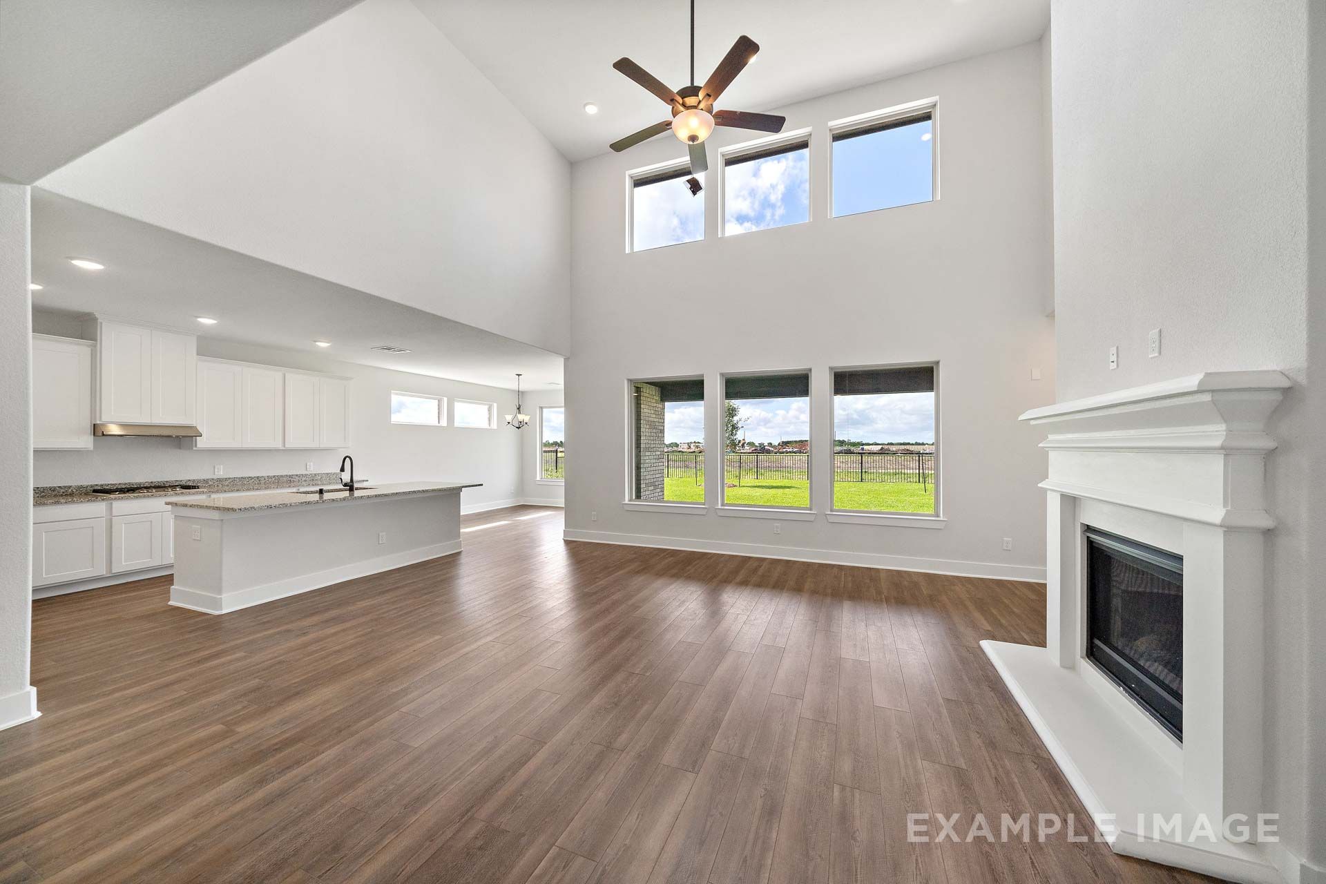 Open-concept great room in The Victoria by Davidson Homes with two-story ceiling, fireplace, white kitchen, and wood-look flooring