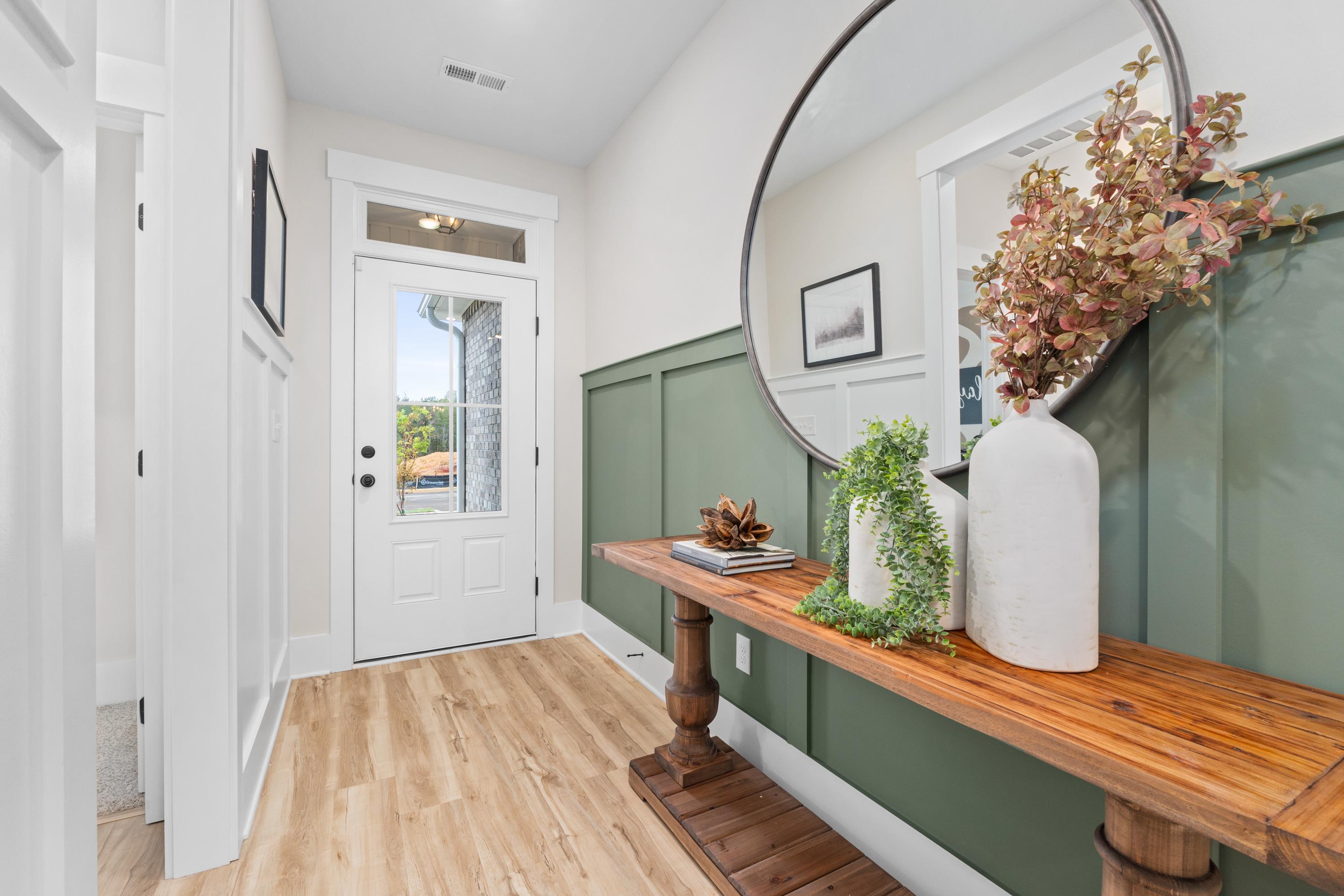 Elegant entryway at Spragins Cove in Huntsville AL with green wainscoted wall, wooden console table, large round mirror, and hardwood floors