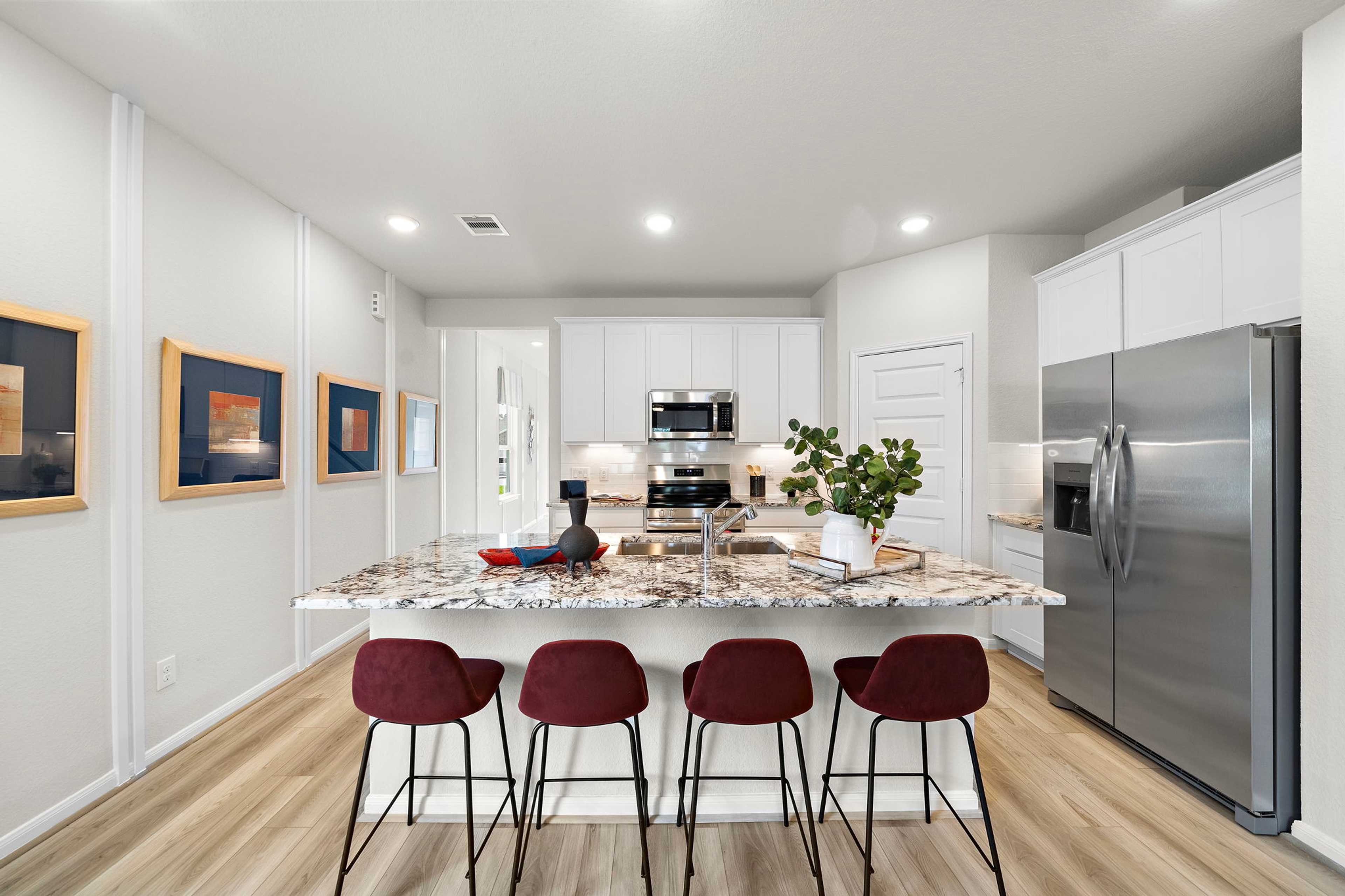 Modern kitchen at Liberty Estates in Cleveland Texas by Davidson Homes featuring white cabinets granite island red bar stools and stainless appliances