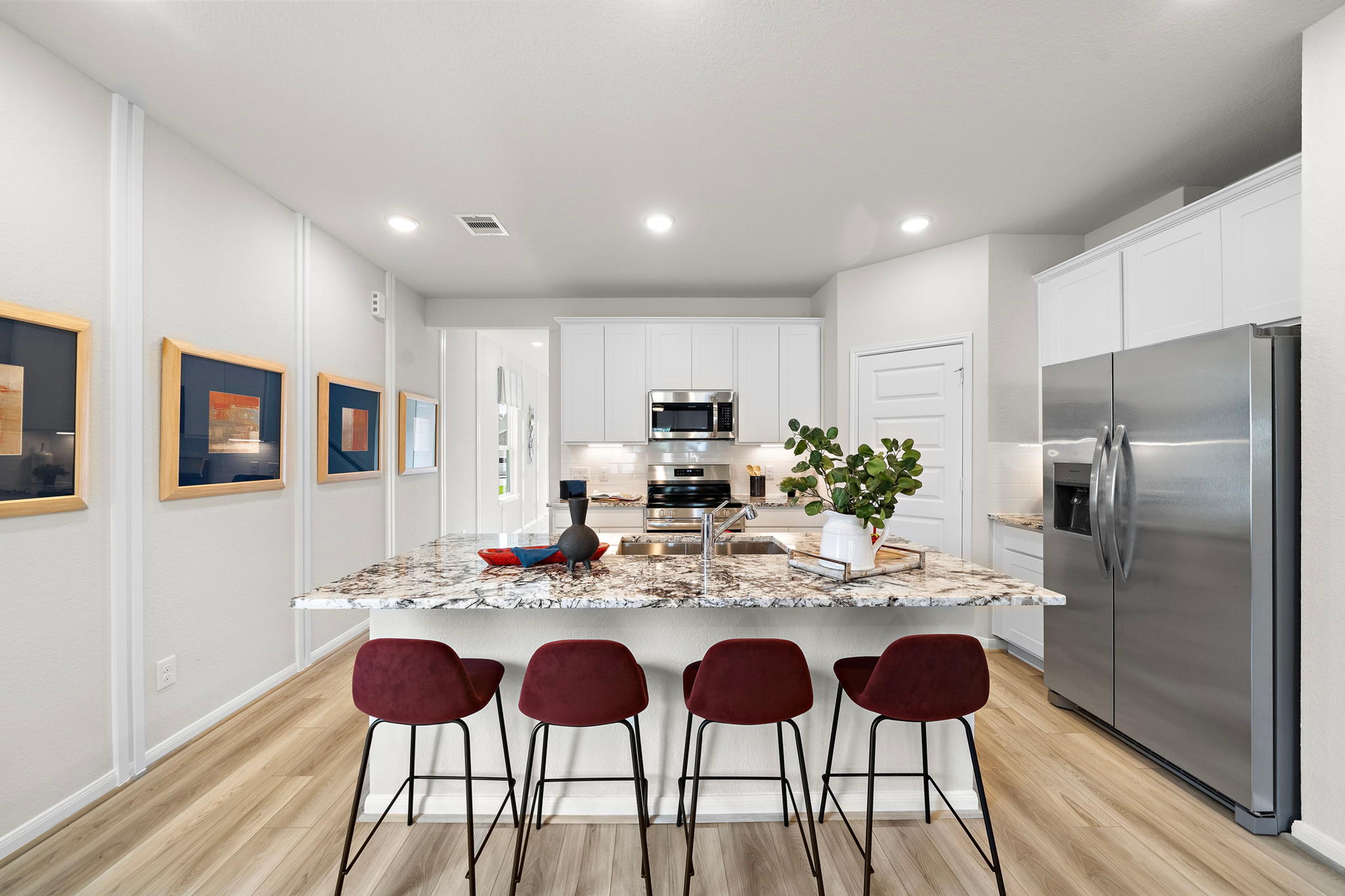 Modern kitchen at Liberty Estates in Cleveland Texas by Davidson Homes featuring white cabinets granite island red bar stools and stainless appliances