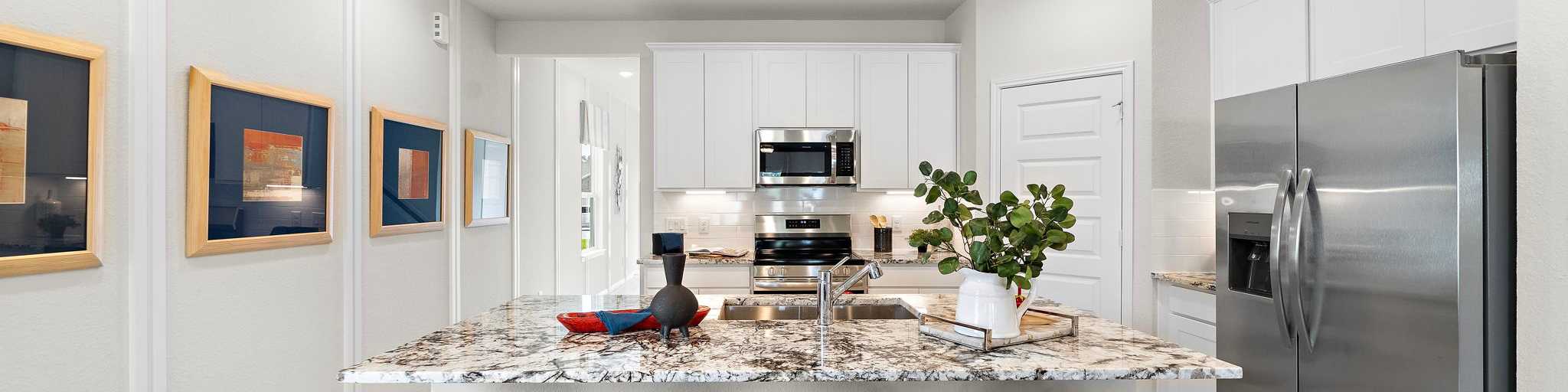 Modern kitchen at Liberty Estates in Cleveland Texas by Davidson Homes featuring white cabinets granite island red bar stools and stainless appliances