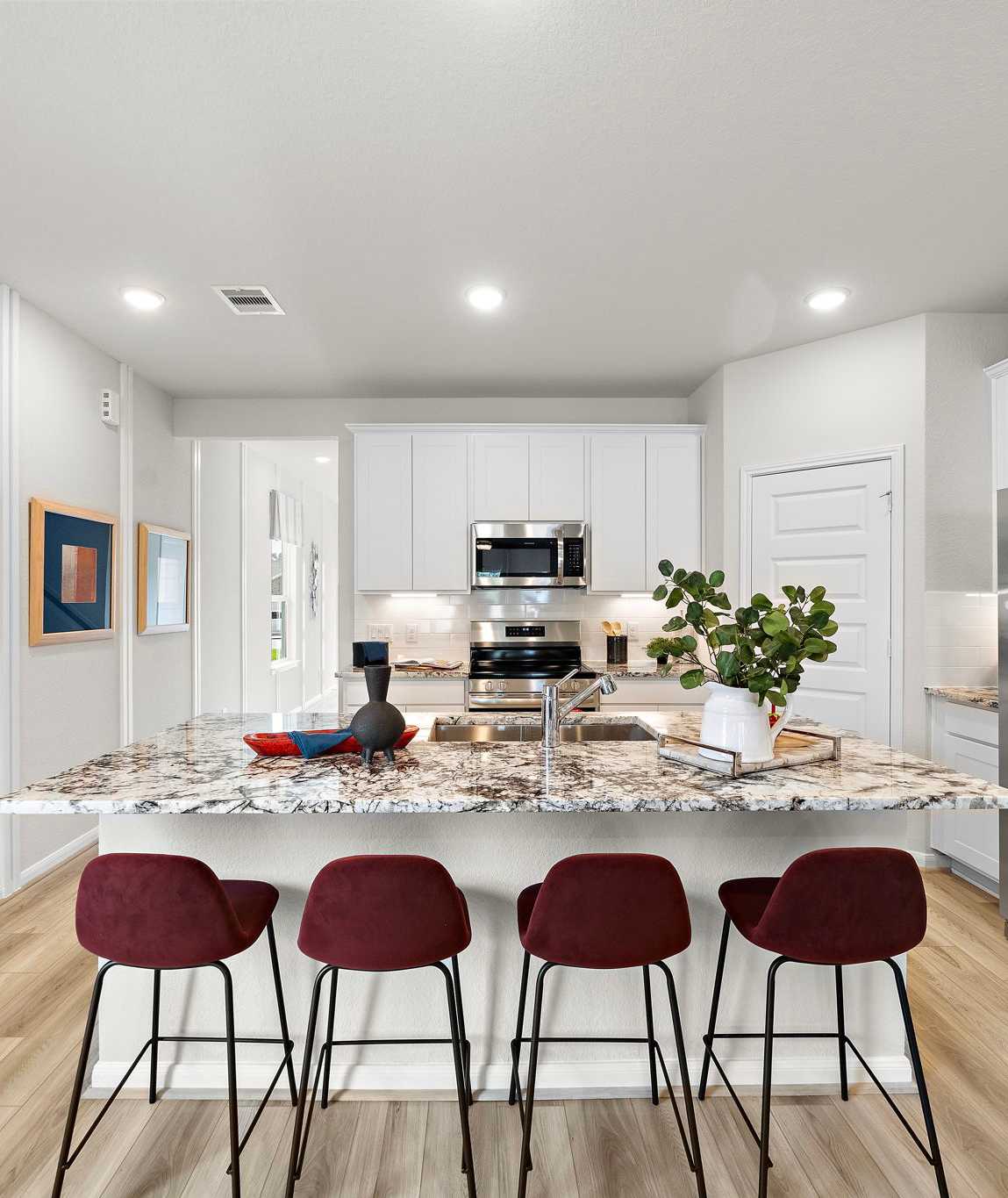 Modern kitchen at Liberty Estates in Cleveland Texas by Davidson Homes featuring white cabinets granite island red bar stools and stainless appliances