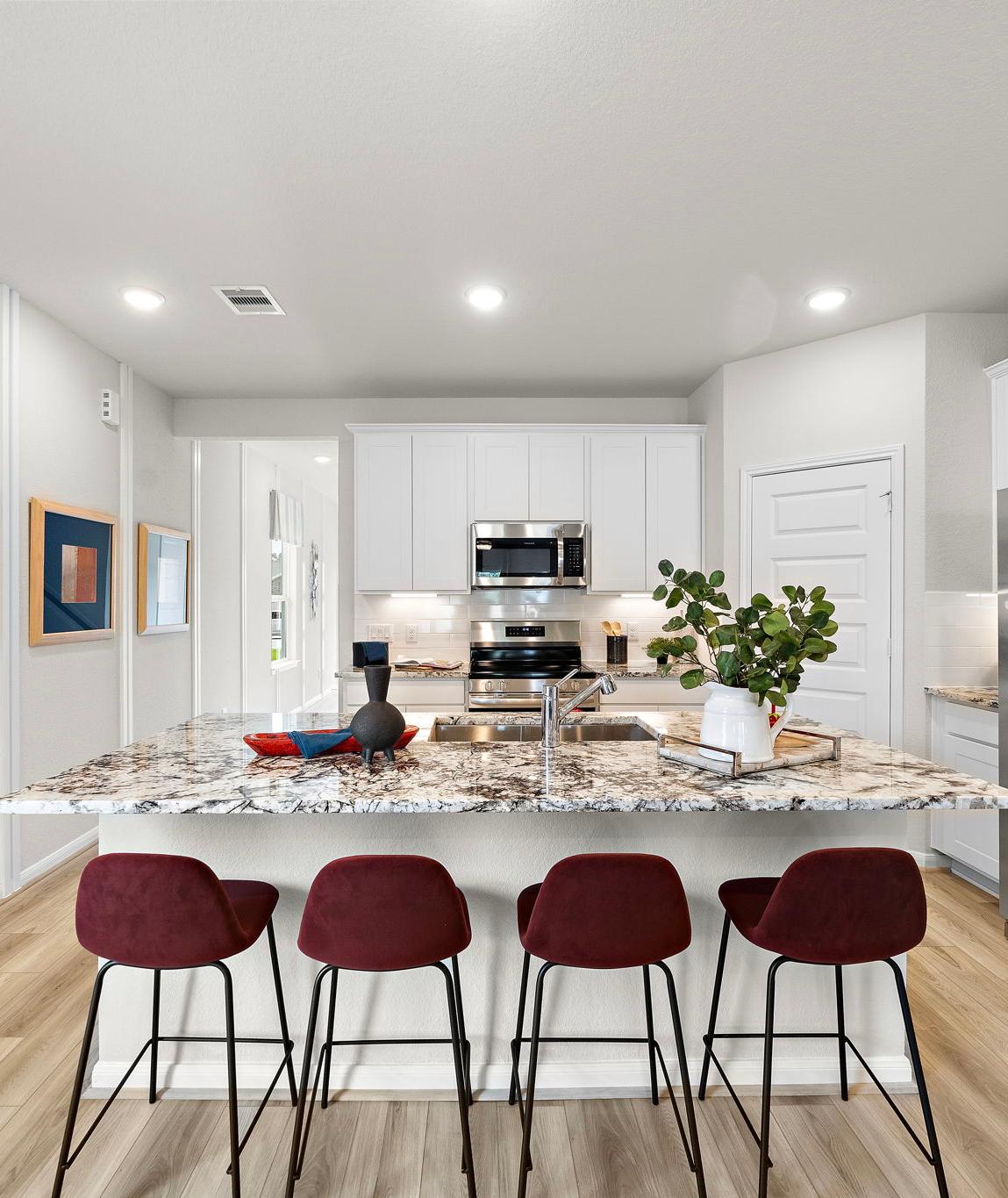 Modern kitchen at Liberty Estates in Cleveland Texas by Davidson Homes featuring white cabinets granite island red bar stools and stainless appliances