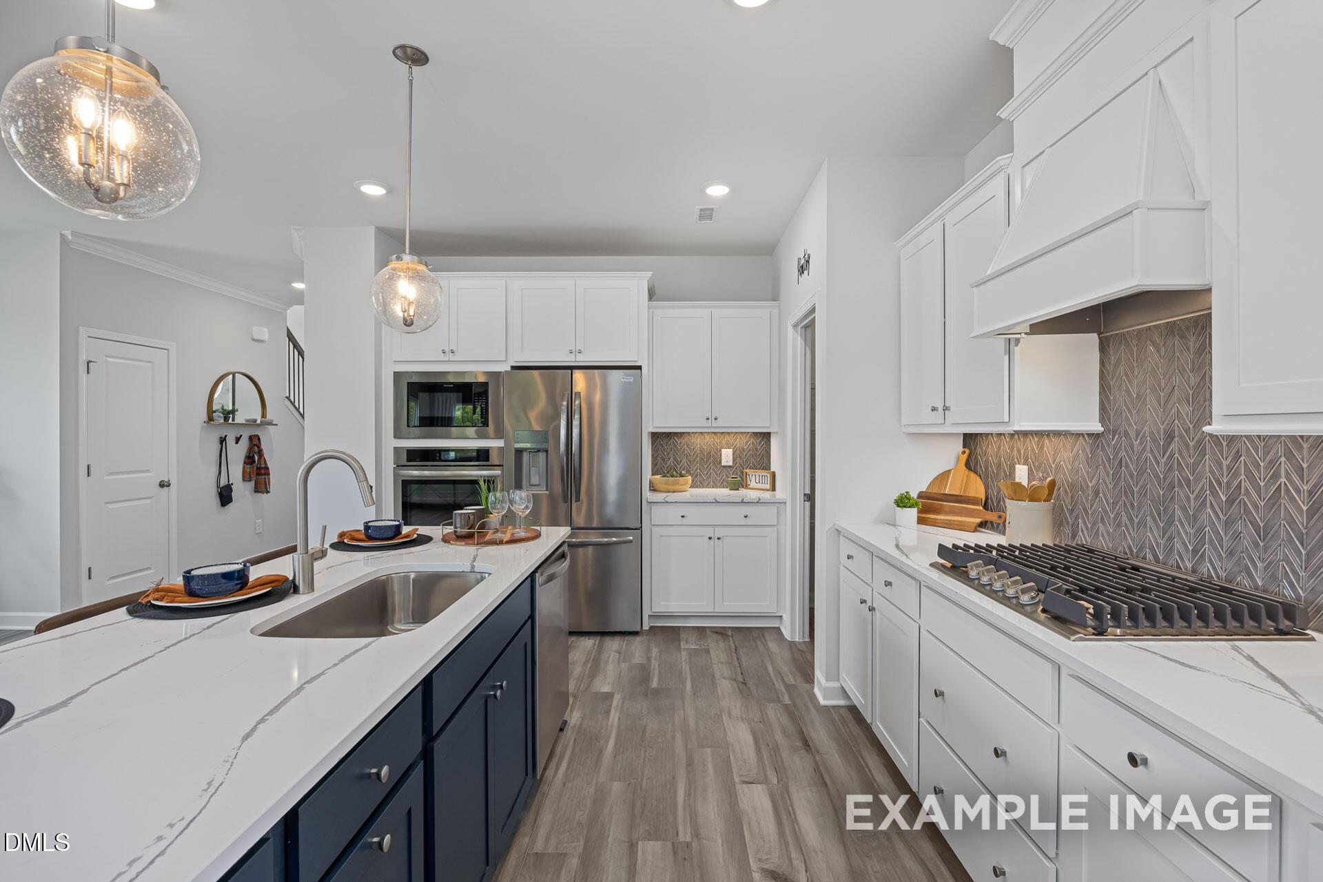 Modern gourmet kitchen with navy island, white cabinets, and stainless appliances in The Adalynn A, Woodland Crossing home.