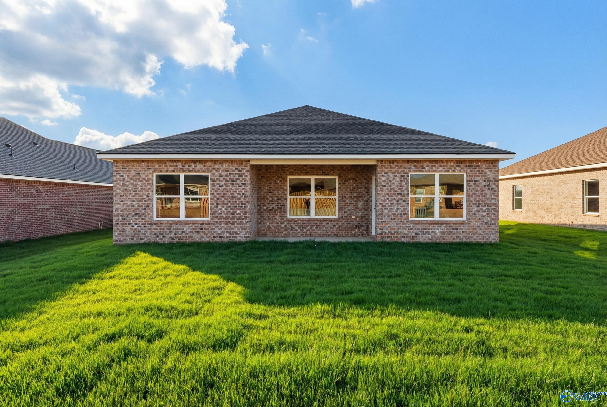 Single-story brick ranch home with gabled roof, triple windows, and lush green lawn in Wood Trail, Toney, Alabama