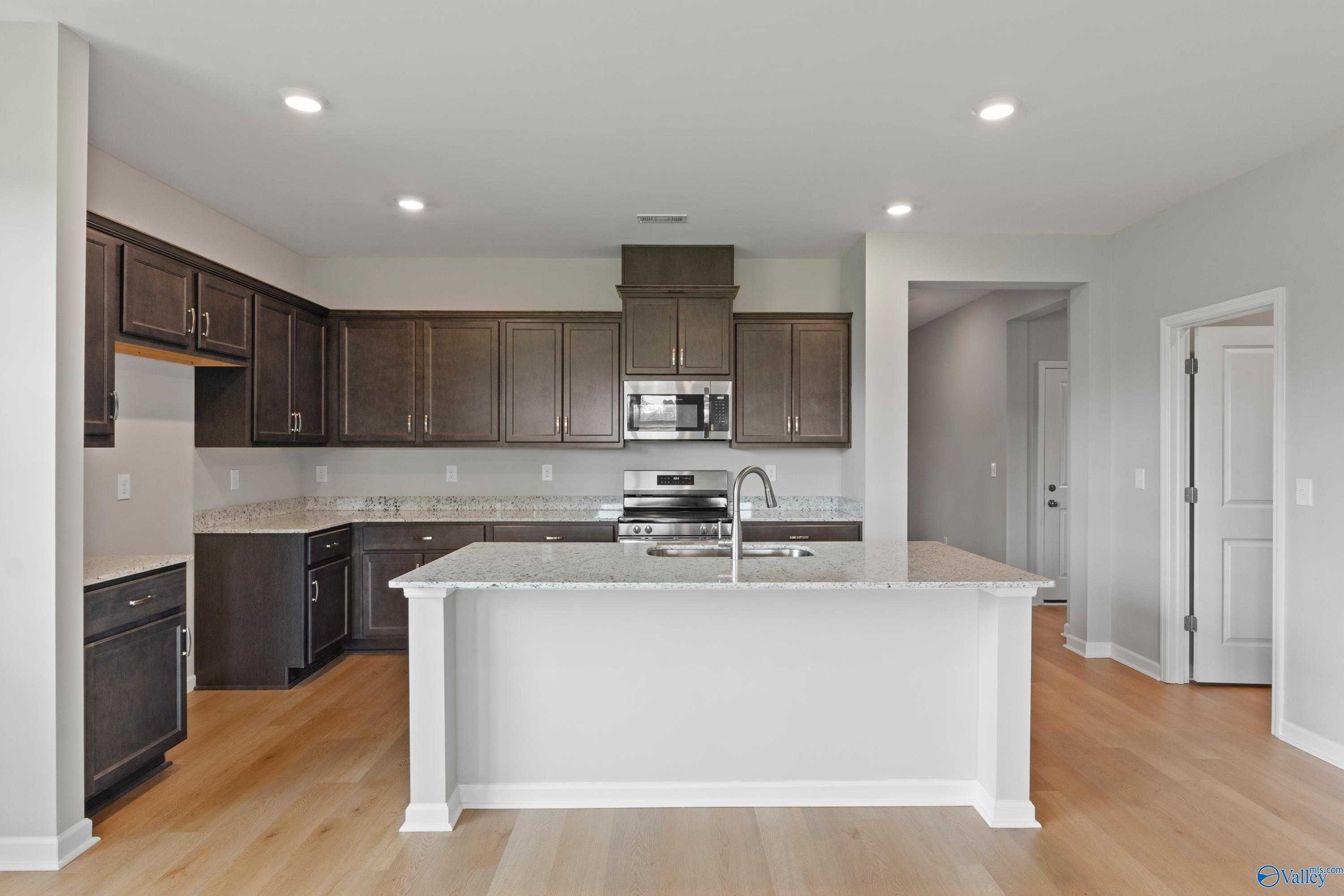Modern kitchen featuring dark wood cabinets, white island with granite countertop and stainless sink in The Aurora 4-bedroom home, Harvest, Alabama