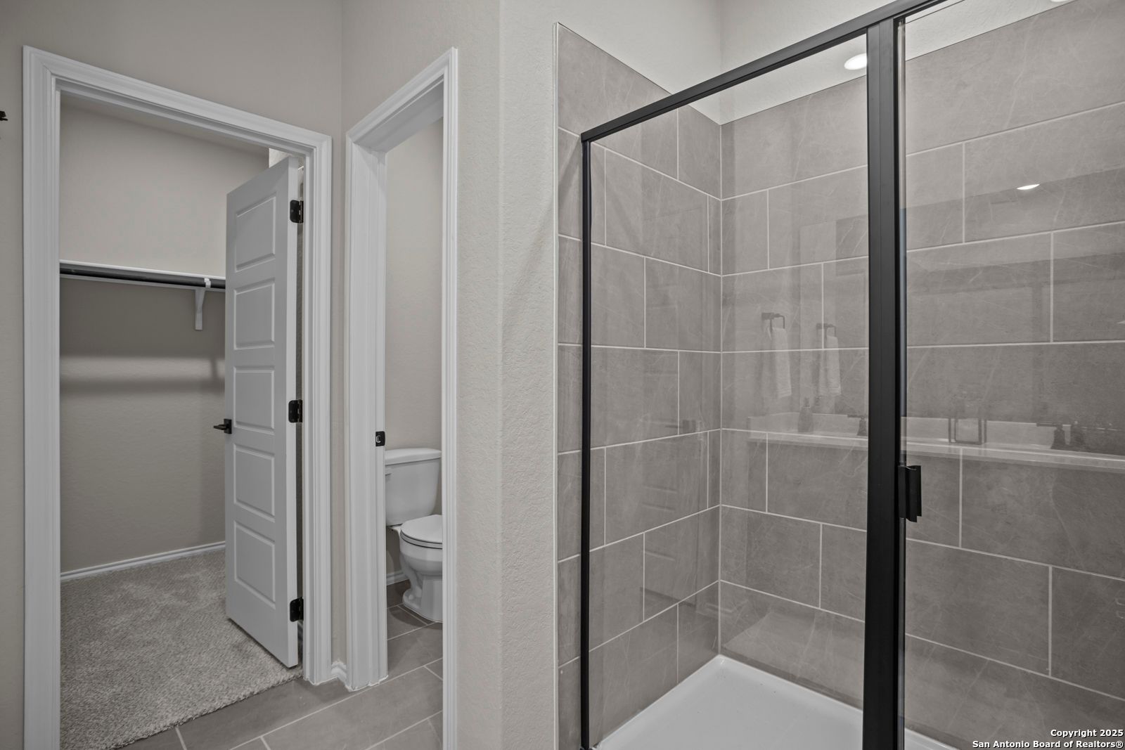 Modern master bathroom with frameless glass walk-in shower, gray tile, toilet, and adjacent closet in The Asheville H, Converse TX