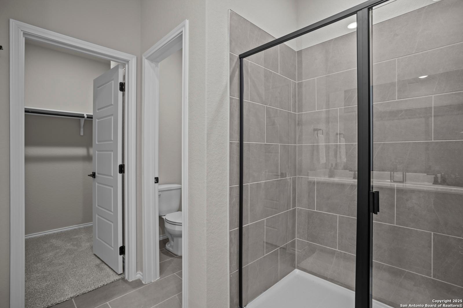 Modern master bathroom with frameless glass walk-in shower, gray tile, toilet, and adjacent closet in The Asheville H, Converse TX