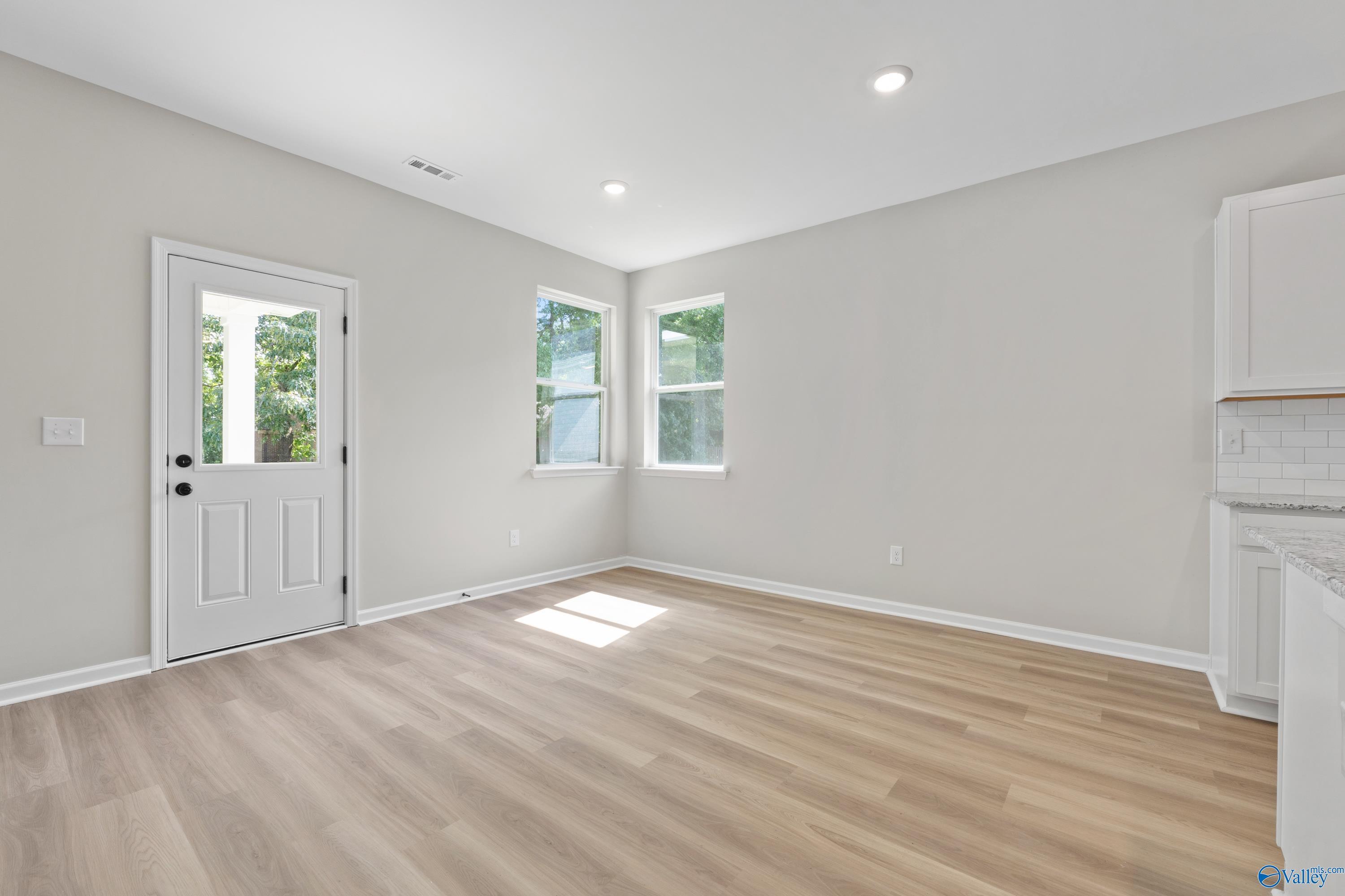 Bright empty living room with large windows, French door to backyard, light gray walls, wood laminate floors in Davidson Homes The Phoenix, Fayetteville, TN