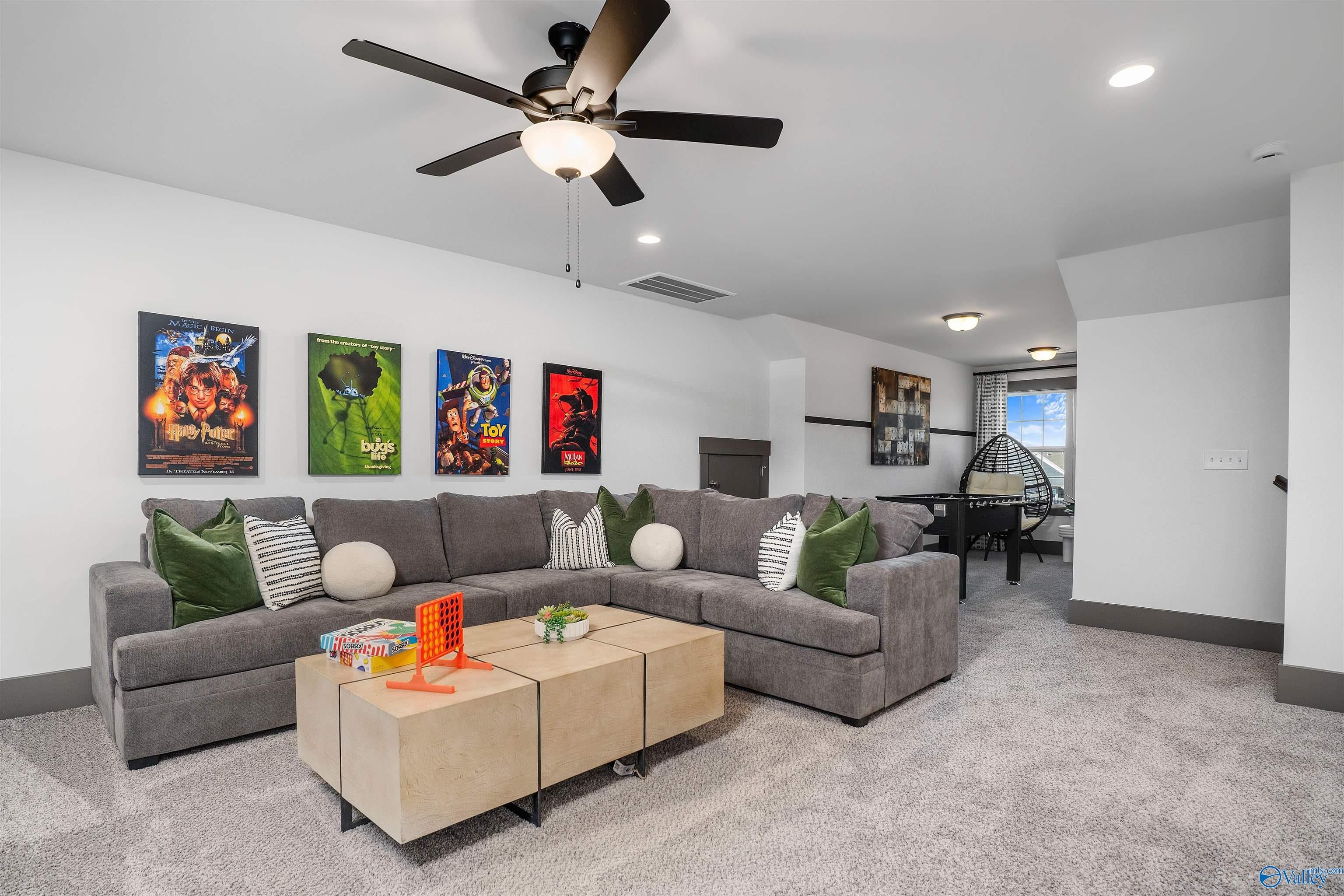 Cozy bonus room with gray sectional sofa, green pillows, superhero posters, board game coffee table, ceiling fans in The Rockford B home, Madison AL