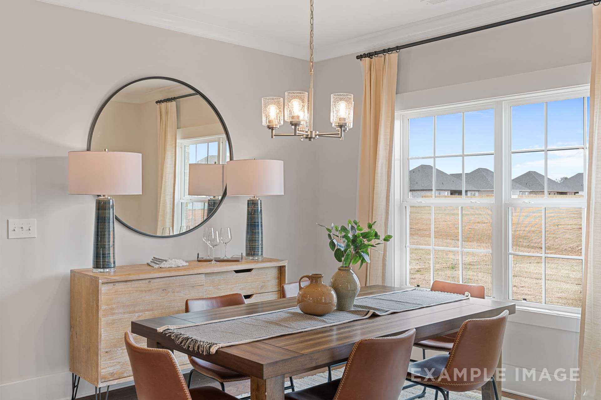 Spacious The Rockford dining room with wooden table, leather chairs, round mirror, chandelier, and large windows overlooking fields