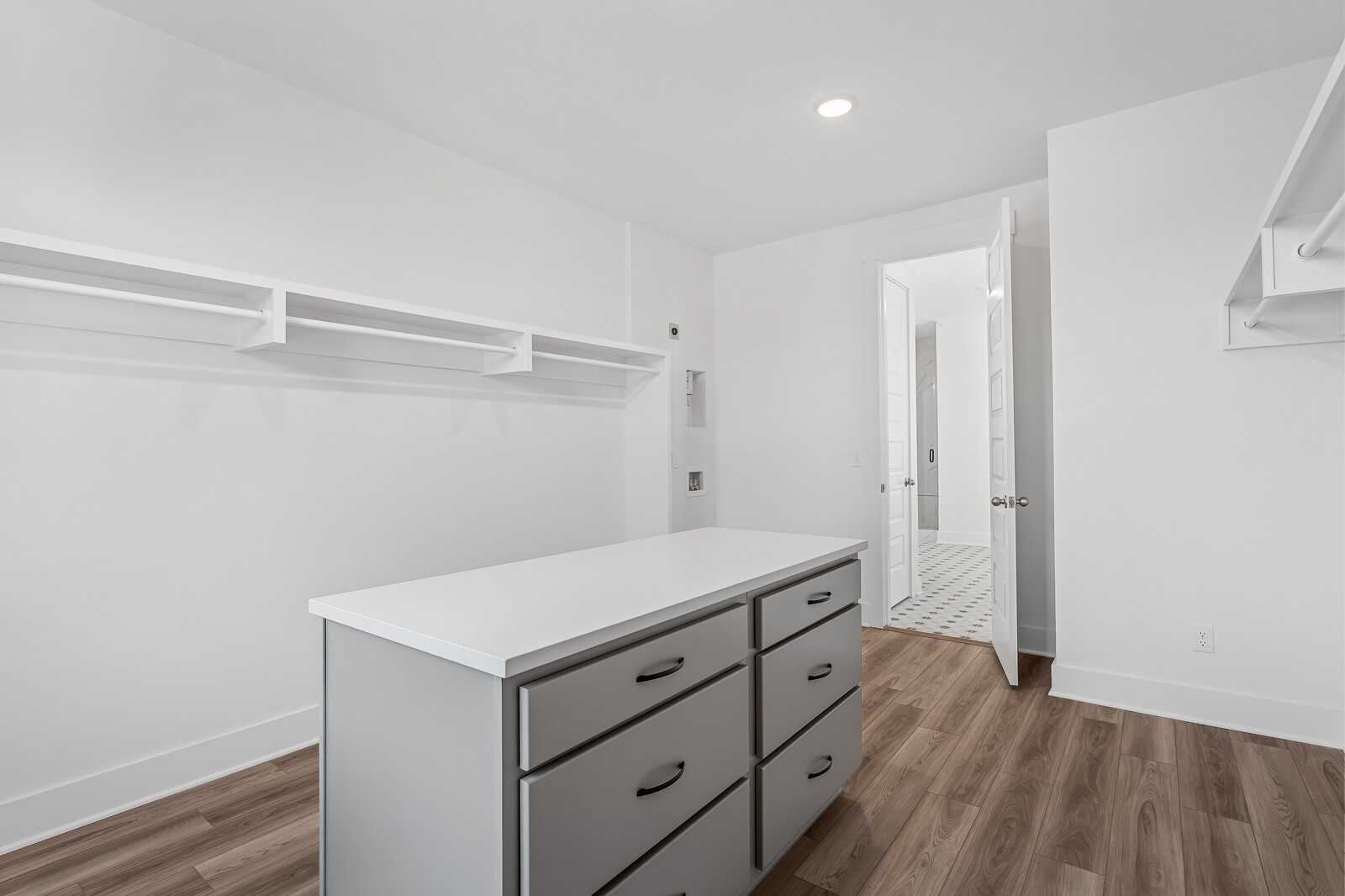 Spacious walk-in closet with white built-in shelving, central island storage, and hardwood floors in Davidson Homes The Alston A, Murfreesboro