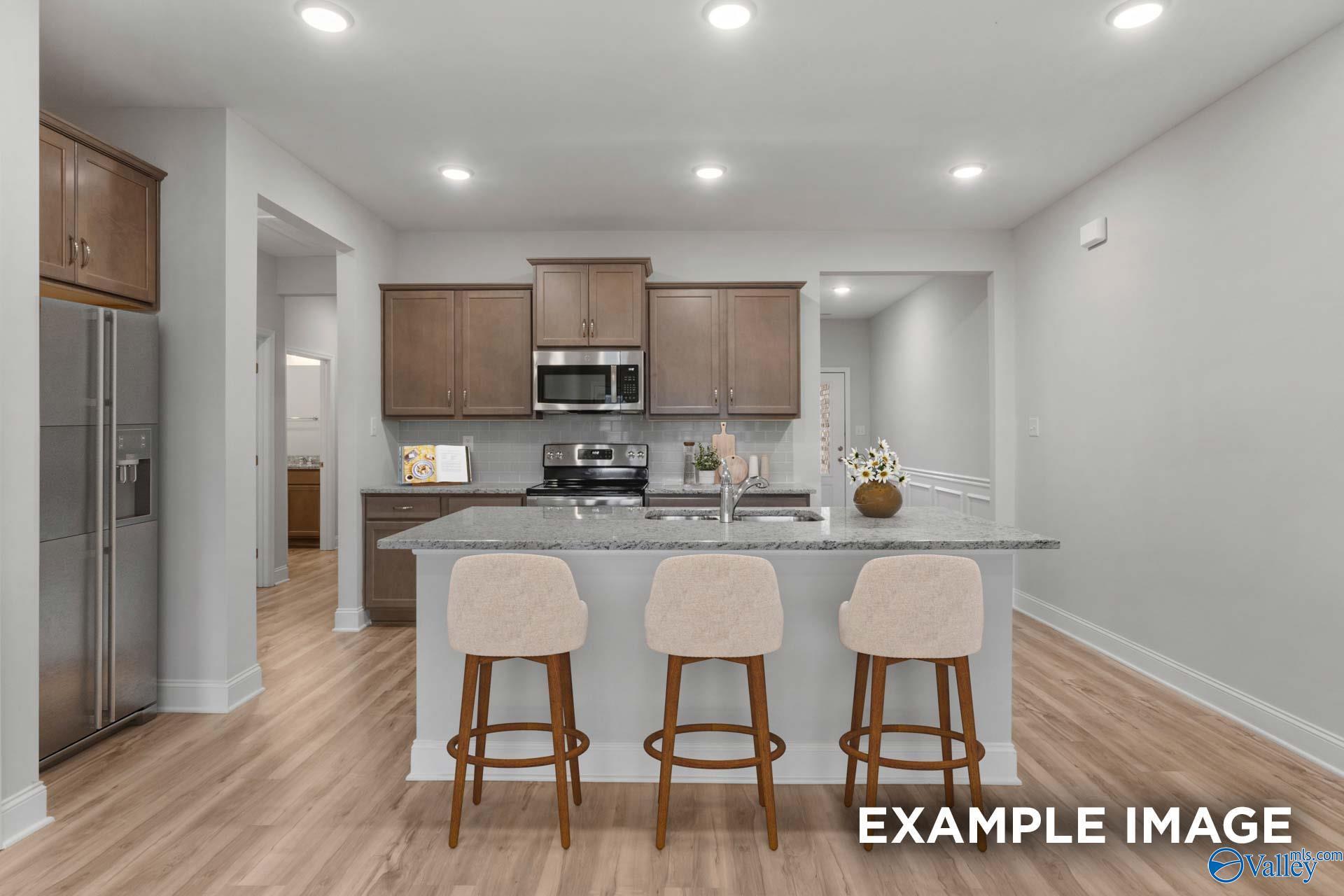 Modern open-concept kitchen with large gray island, bar stools, stainless appliances, and wood cabinets in Davidson Homes Cumberland B, Decatur AL