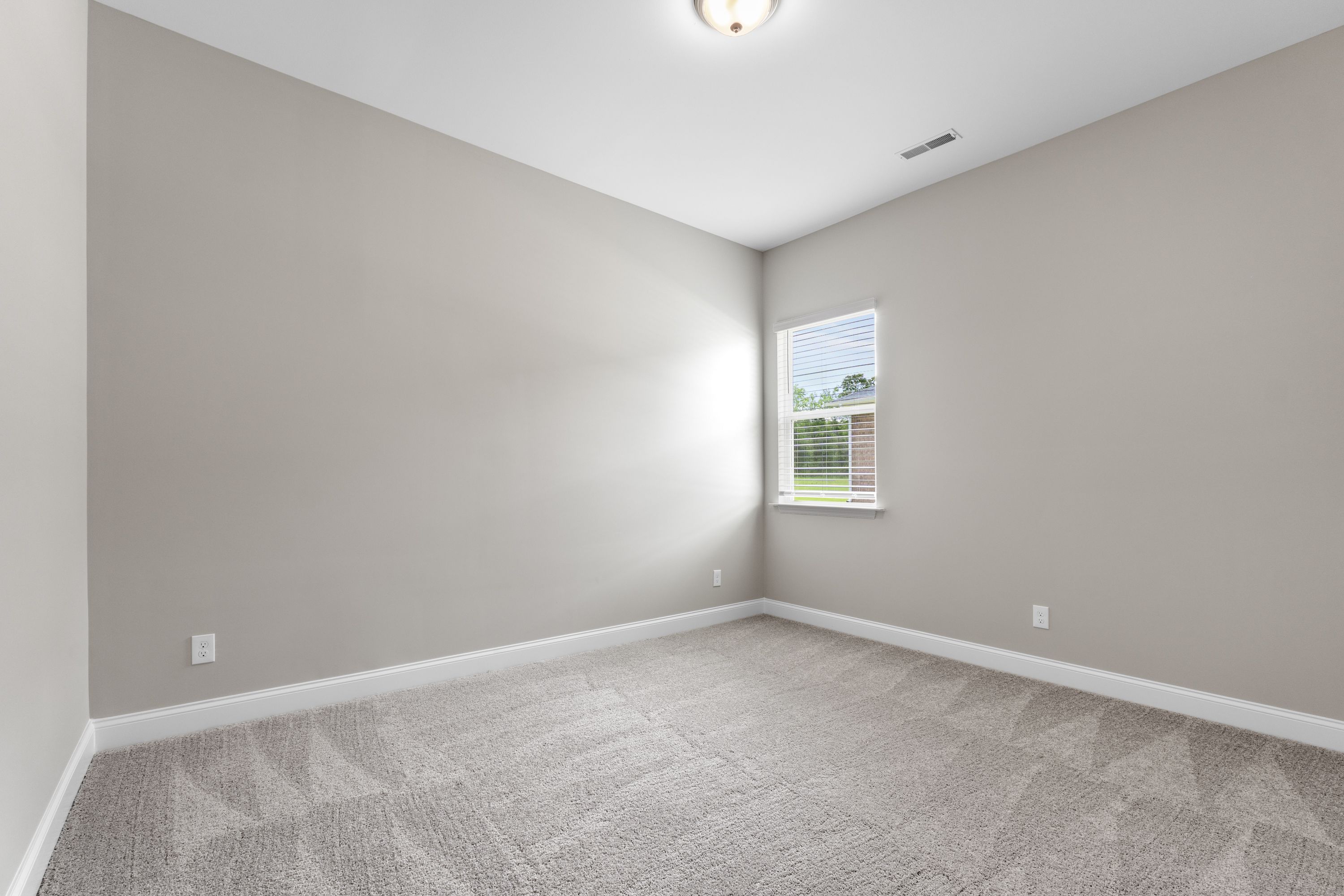 Spacious bedroom interior in The Arcadia E home with light gray walls, beige carpet, large window, and soft natural light