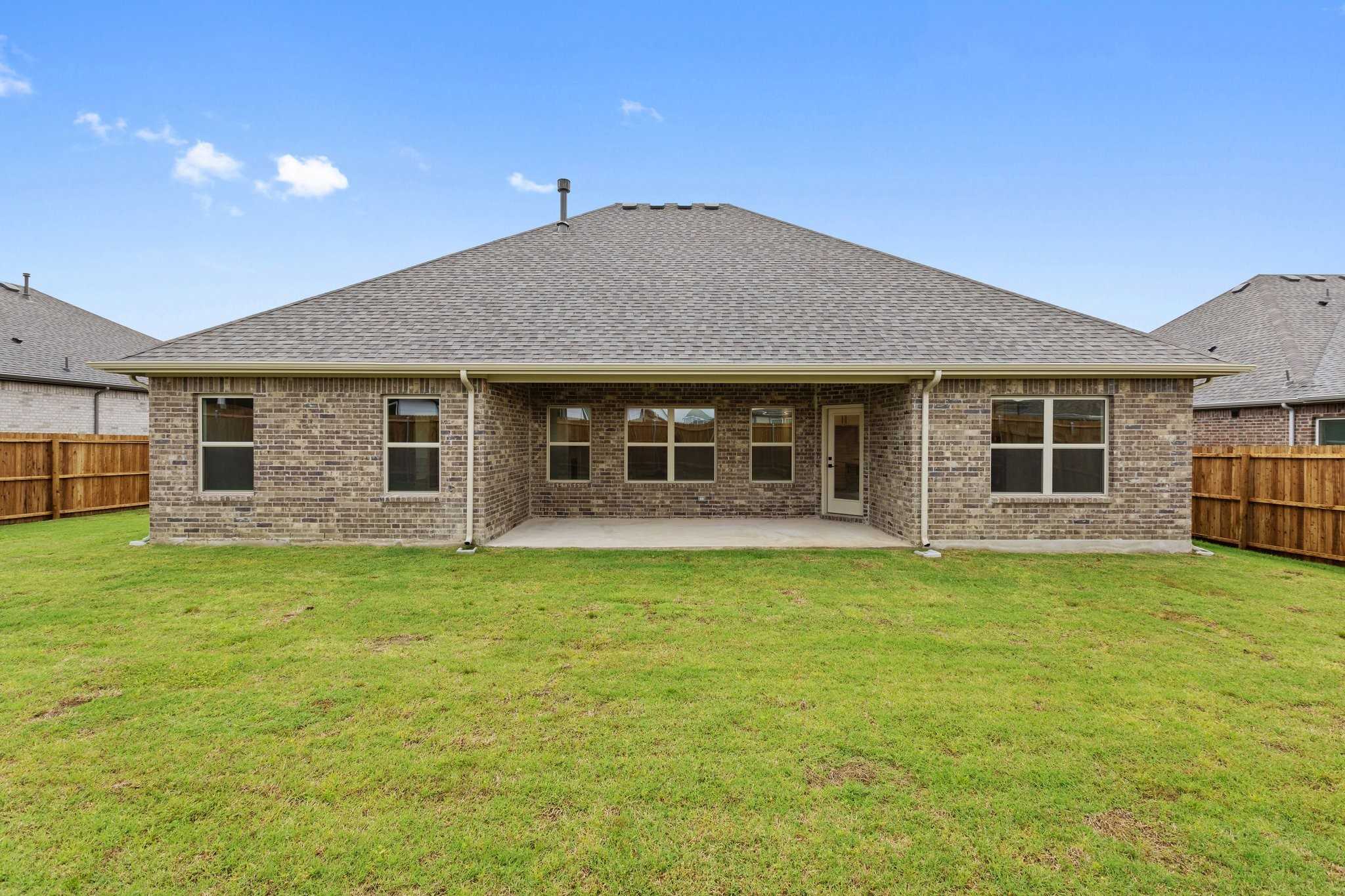 Back view of The Rockford C single-story home with brick exterior, covered patio, large windows, lush green yard, and wood fence in Waverly Estates, Josephine, Texas