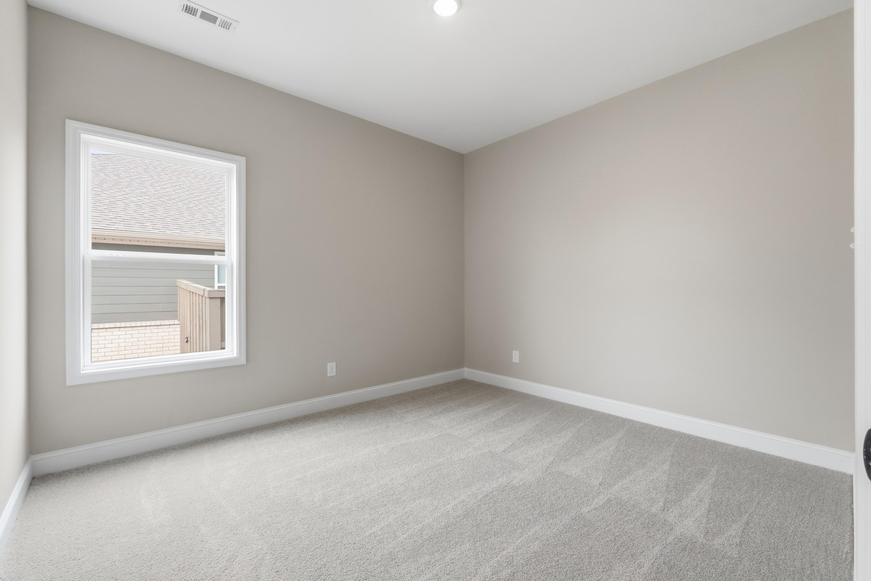 Spacious bedroom in The Rockford home design by Davidson Homes, Cullman AL, with beige walls, carpet floors, large window