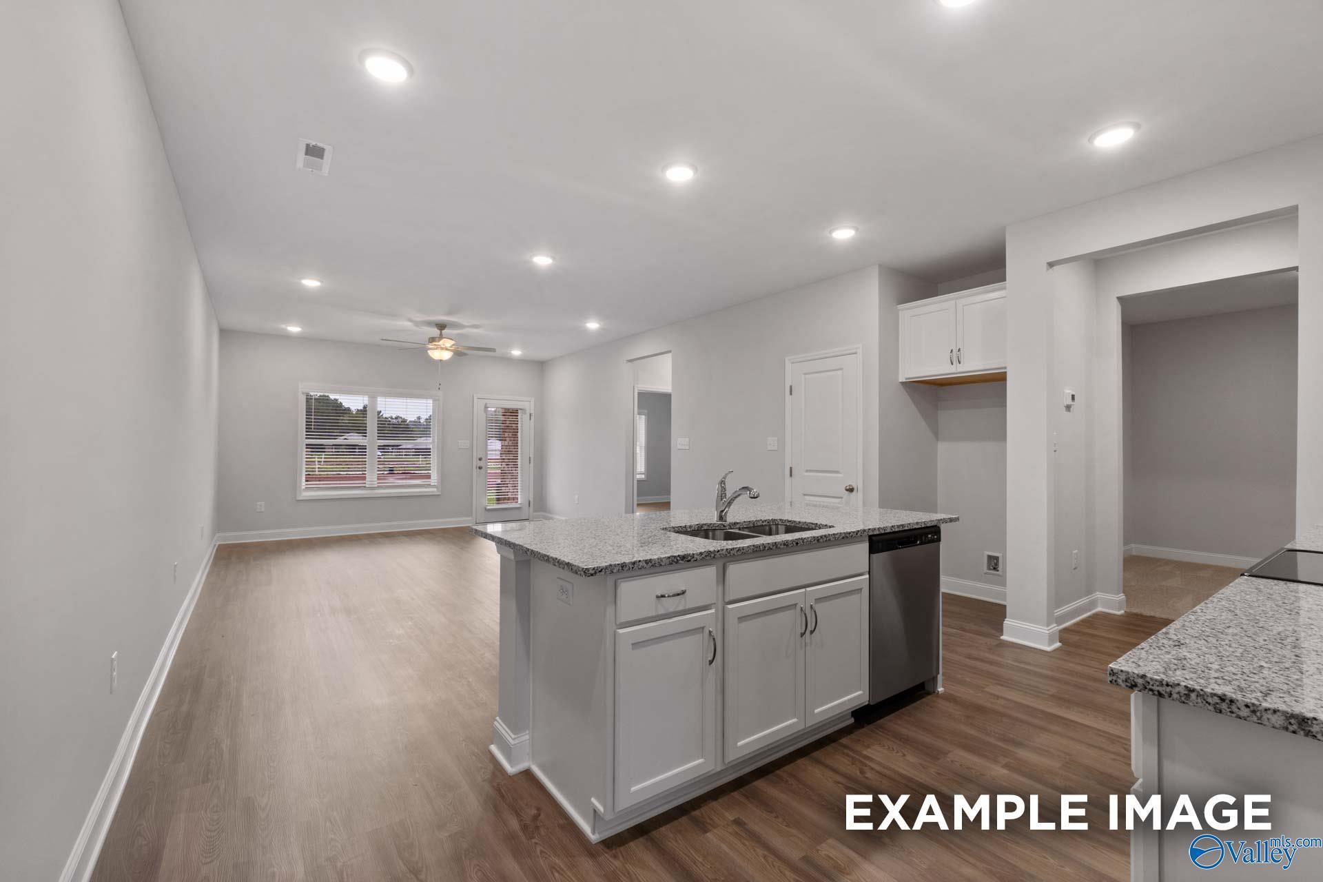 Modern open-concept kitchen with granite island, white cabinets, and hardwood floors in Davidson Homes Cumberland B, Decatur, AL