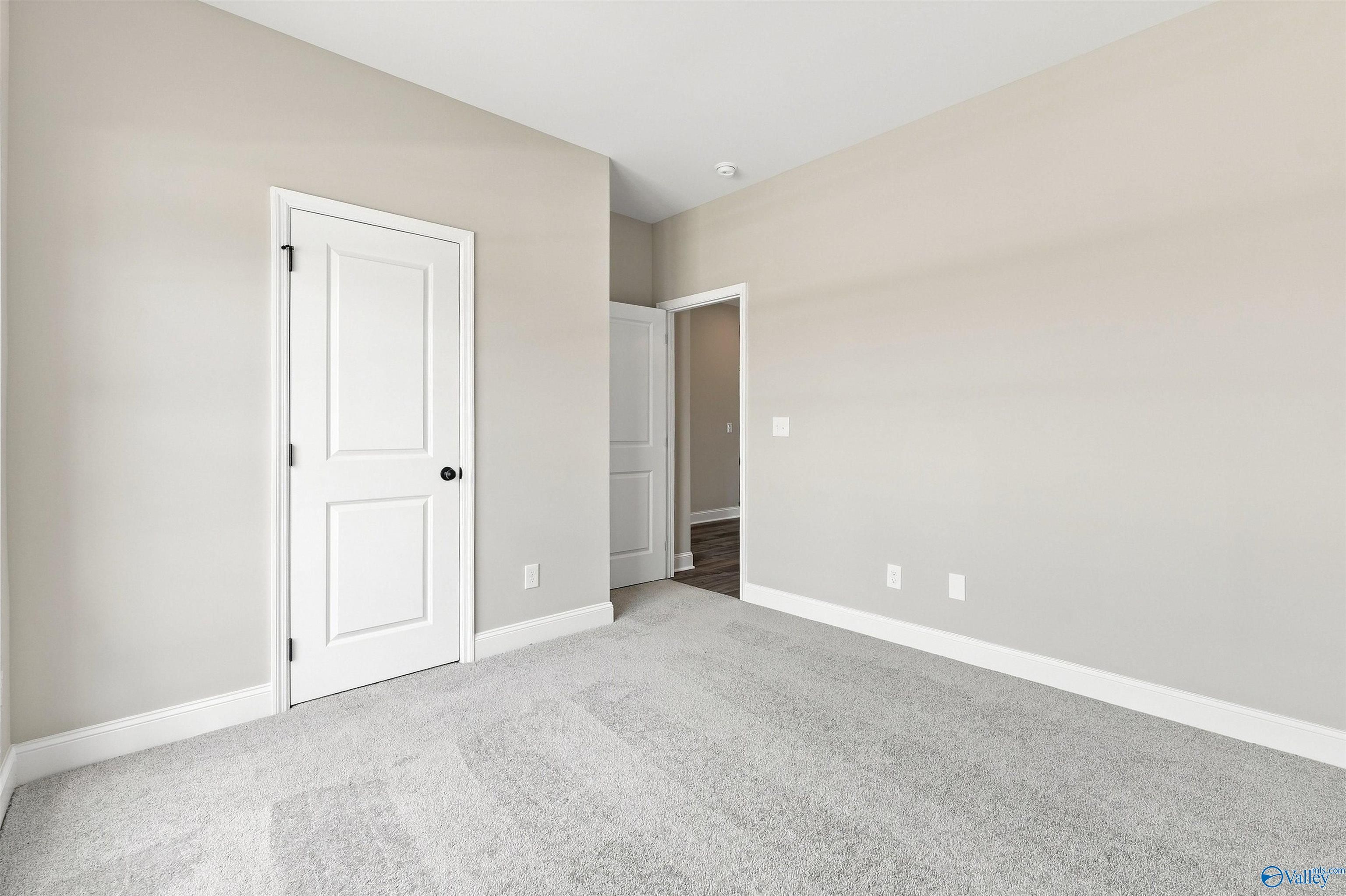 Bright neutral bedroom with plush gray carpet, white doors, and beige walls in Davidson Homes The Franklin C, Wood Trail, Toney, AL