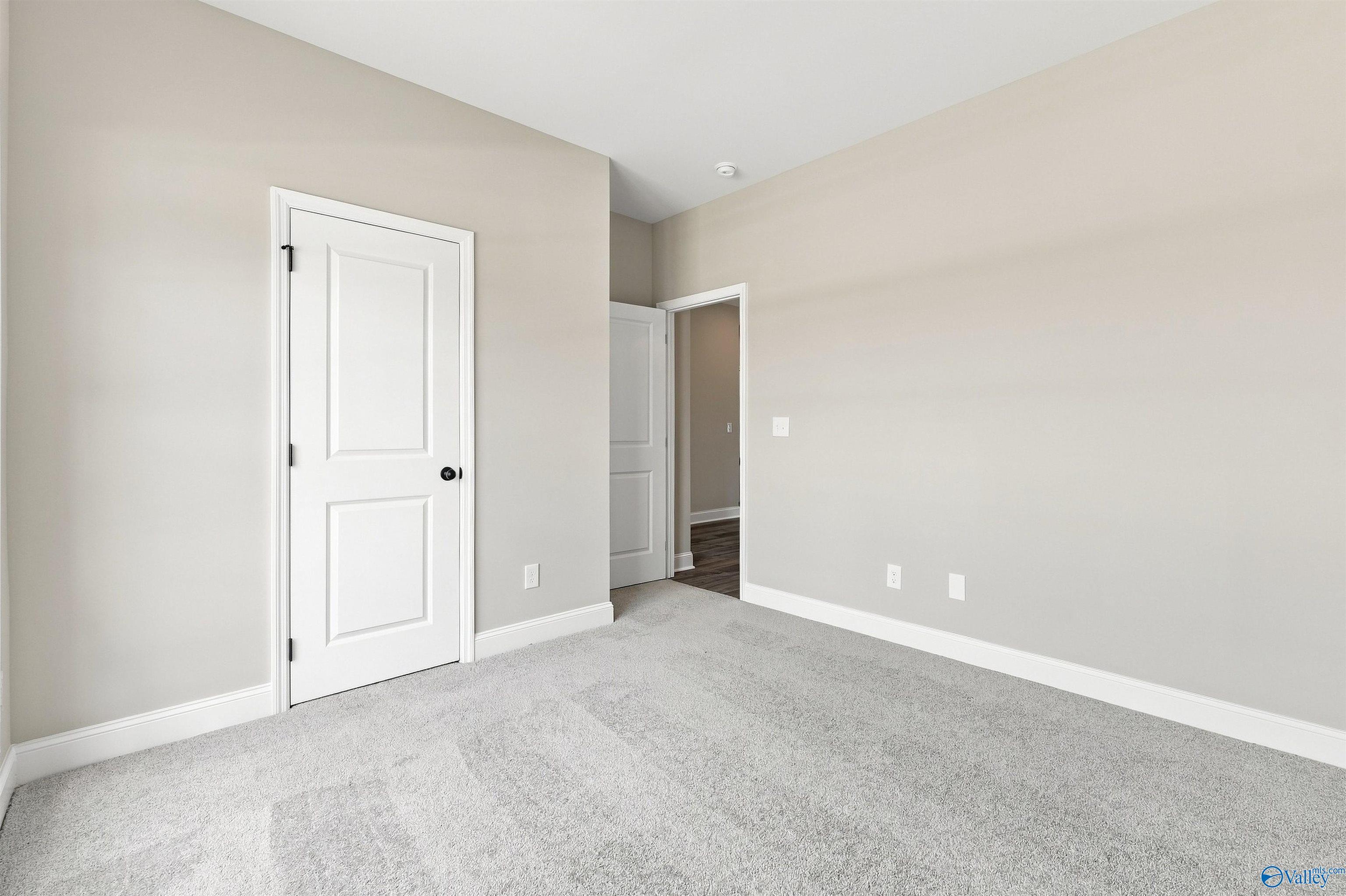 Bright neutral bedroom with plush gray carpet, white doors, and beige walls in Davidson Homes The Franklin C, Wood Trail, Toney, AL