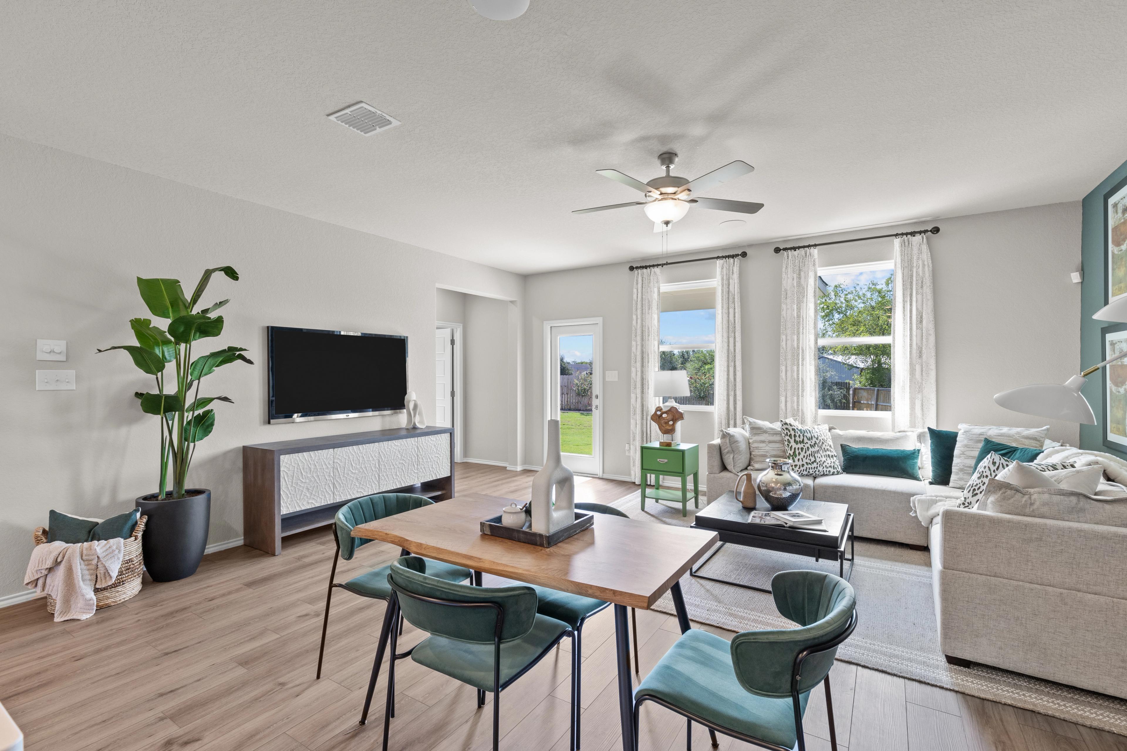Open-concept living and dining room at Comanche Ridge in San Antonio TX by Davidson Homes featuring hardwood floors, beige sofa, and large windows