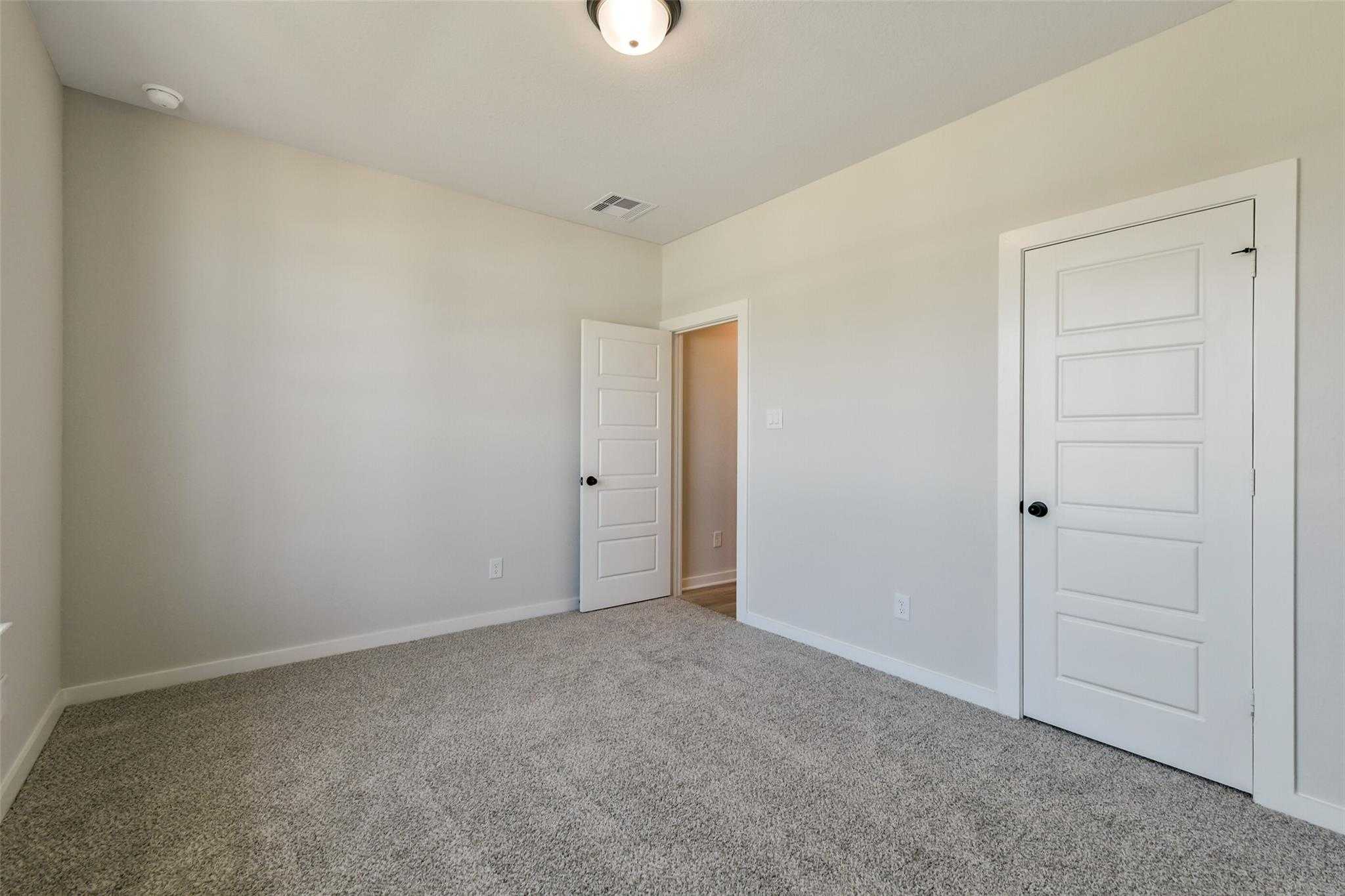 Spacious secondary bedroom with beige carpet, white doors, and adjacent bath in Davidson Homes The Daphne H, Crosby Texas