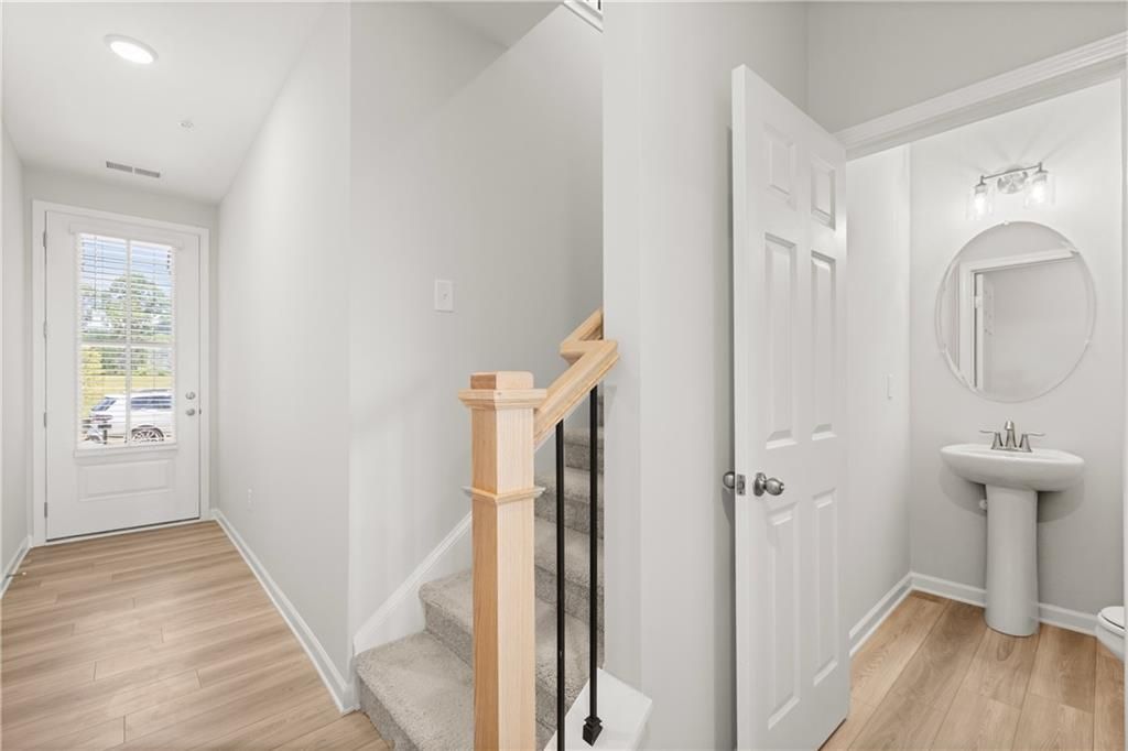 Bright entryway with wood-style flooring, carpeted staircase, and powder room in The Wake B floor plan, Cumming, Georgia.