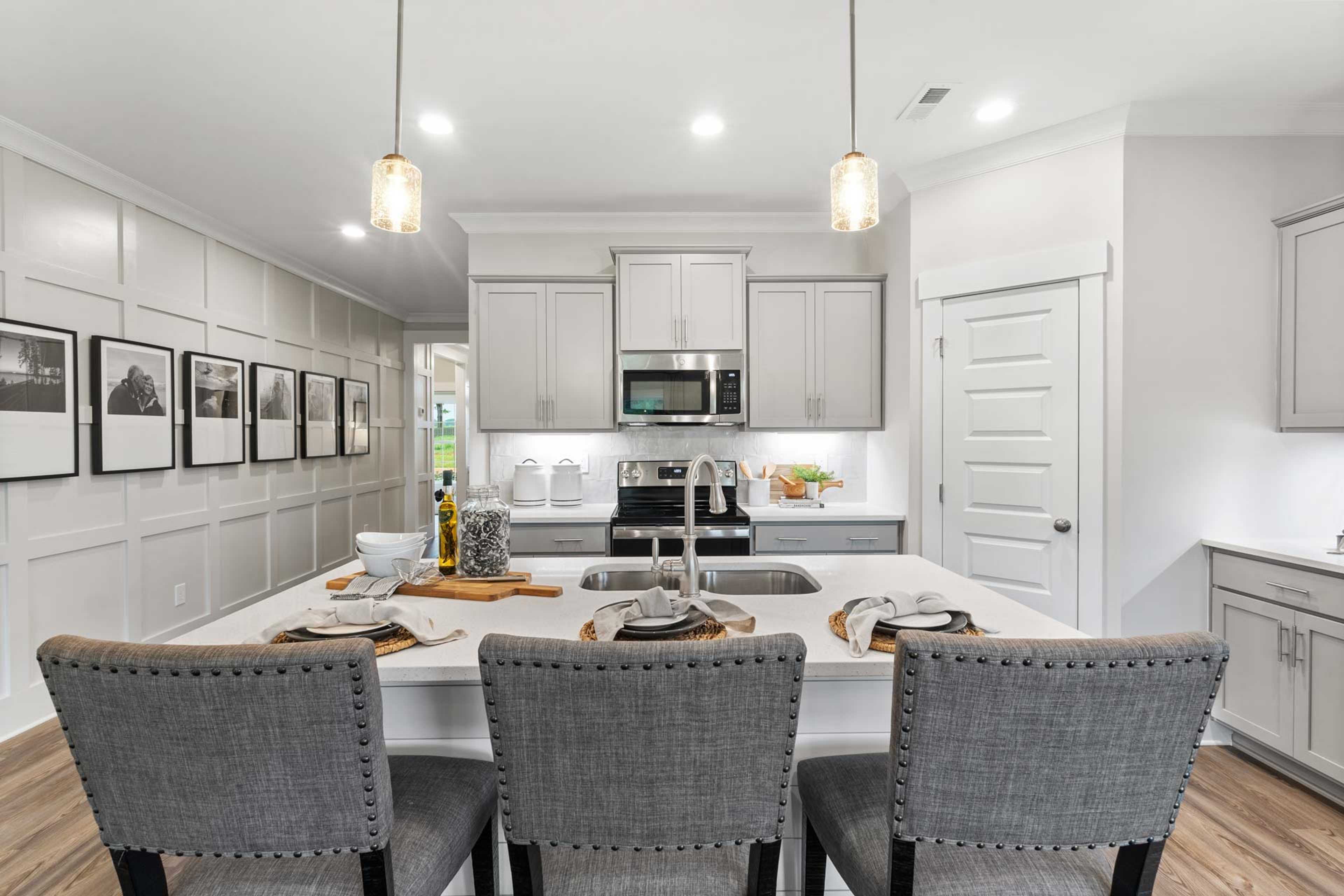 Modern kitchen in The Meadows Athens Alabama featuring white shaker cabinets, large island with sink, gray bar stools, stainless appliances