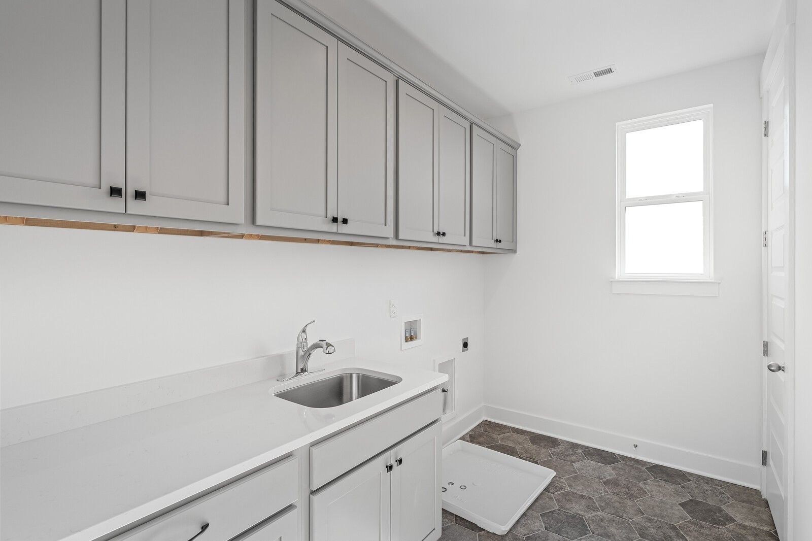 Modern laundry room featuring gray upper cabinets, white countertop sink, and washer space in Davidson Homes The Alston A, Murfreesboro
