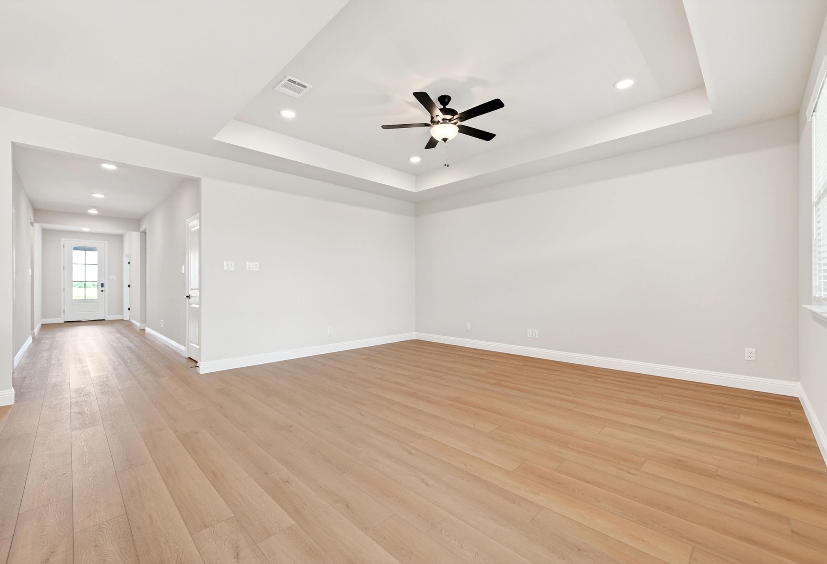 Spacious open-concept living area in The Holly M floor plan featuring a tray ceiling, ceiling fan, and wood-style flooring.