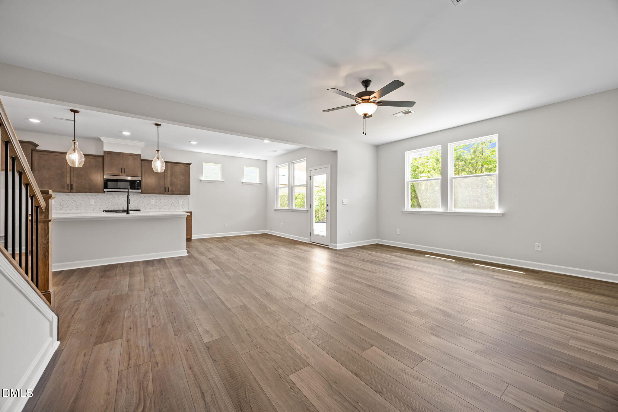 Open-concept living area with hardwood floors, kitchen island, subway tile backsplash, and large windows in Davidson Homes The Willow D, Wendell, NC