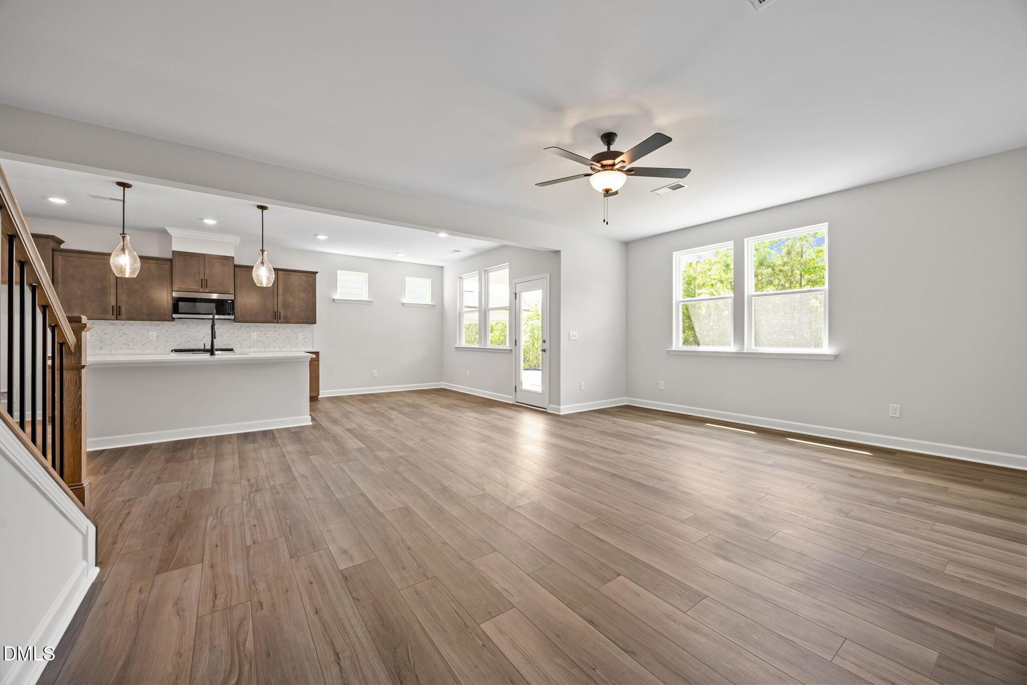 Open-concept living area with hardwood floors, kitchen island, subway tile backsplash, and large windows in Davidson Homes The Willow D, Wendell, NC