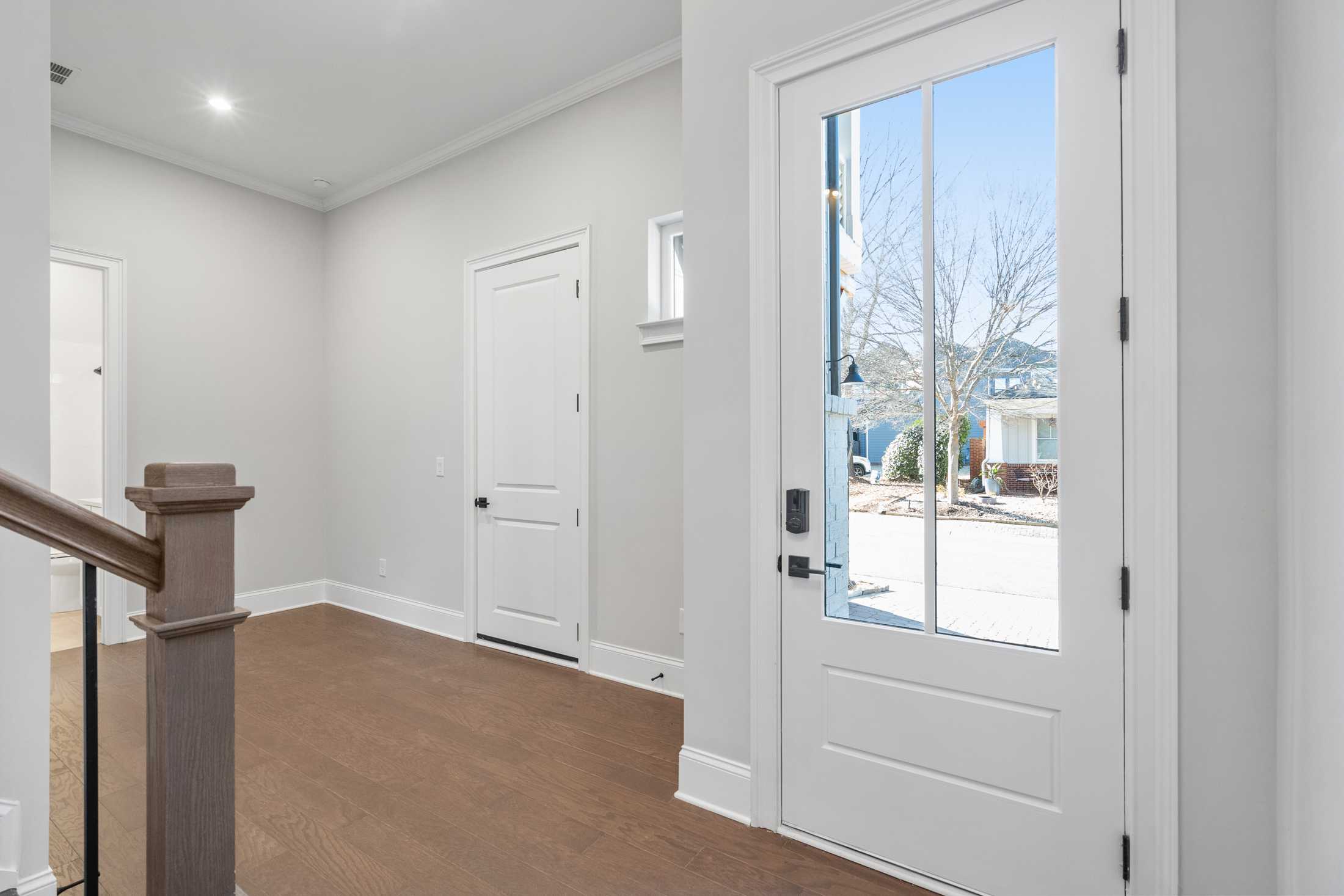 Bright foyer in The Seaside Davidson Homes design featuring light gray walls, hardwood floors, wooden staircase, and glass front door with outdoor view