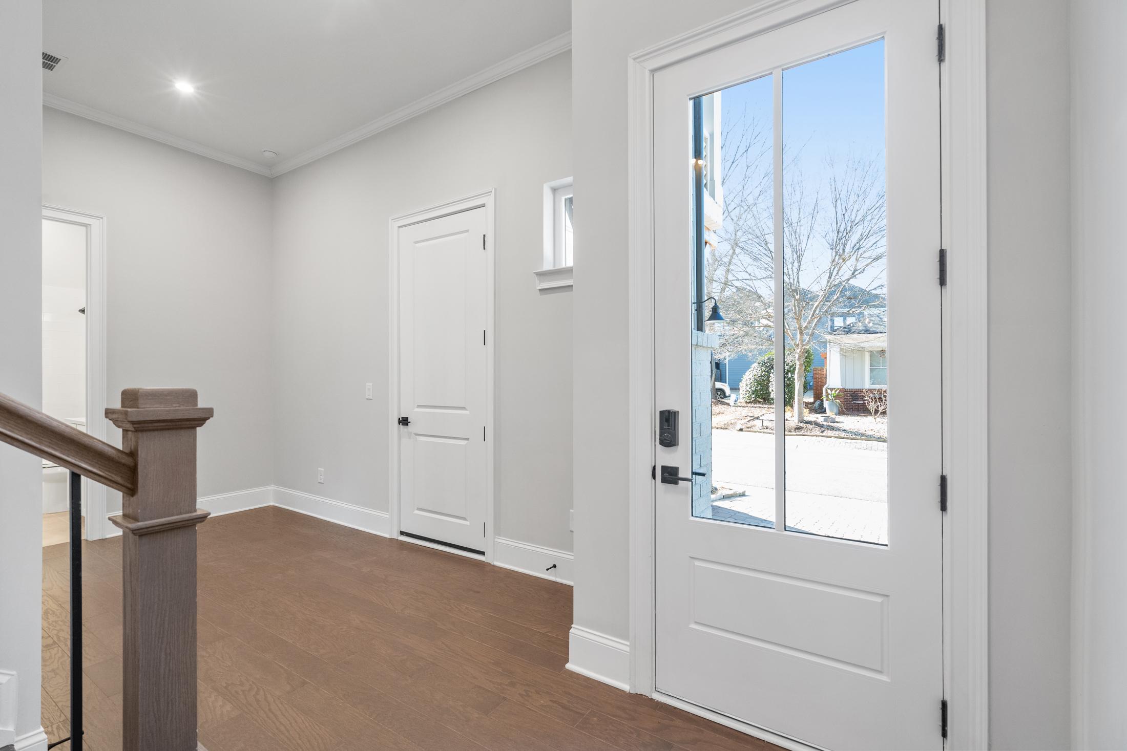 Bright foyer in The Seaside Davidson Homes design featuring light gray walls, hardwood floors, wooden staircase, and glass front door with outdoor view