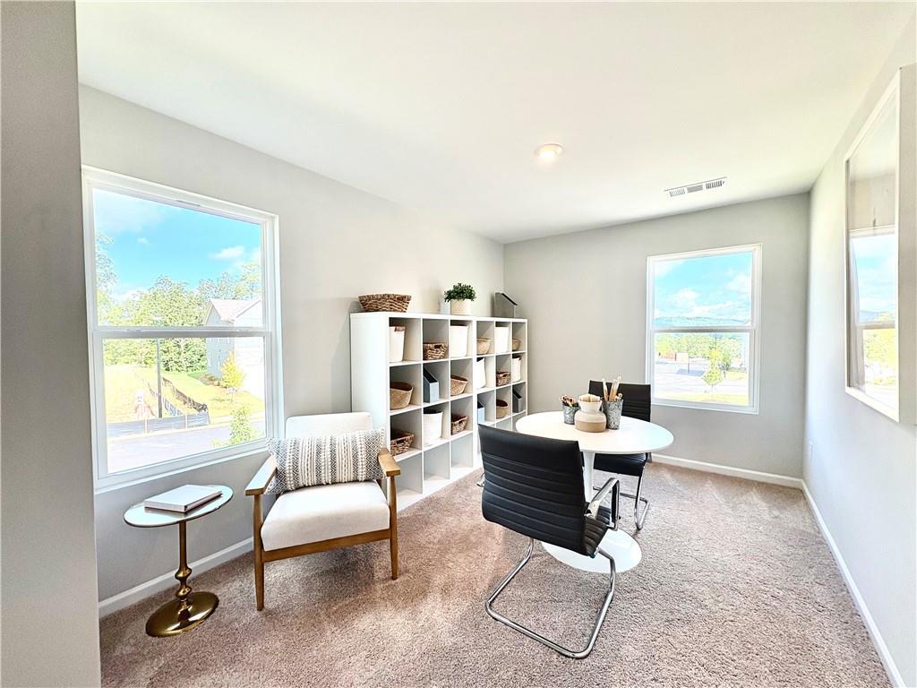 Bright home office with white bookshelves, round table, armchair, and large windows in Davidson Homes The Monroe A, Emerson, GA