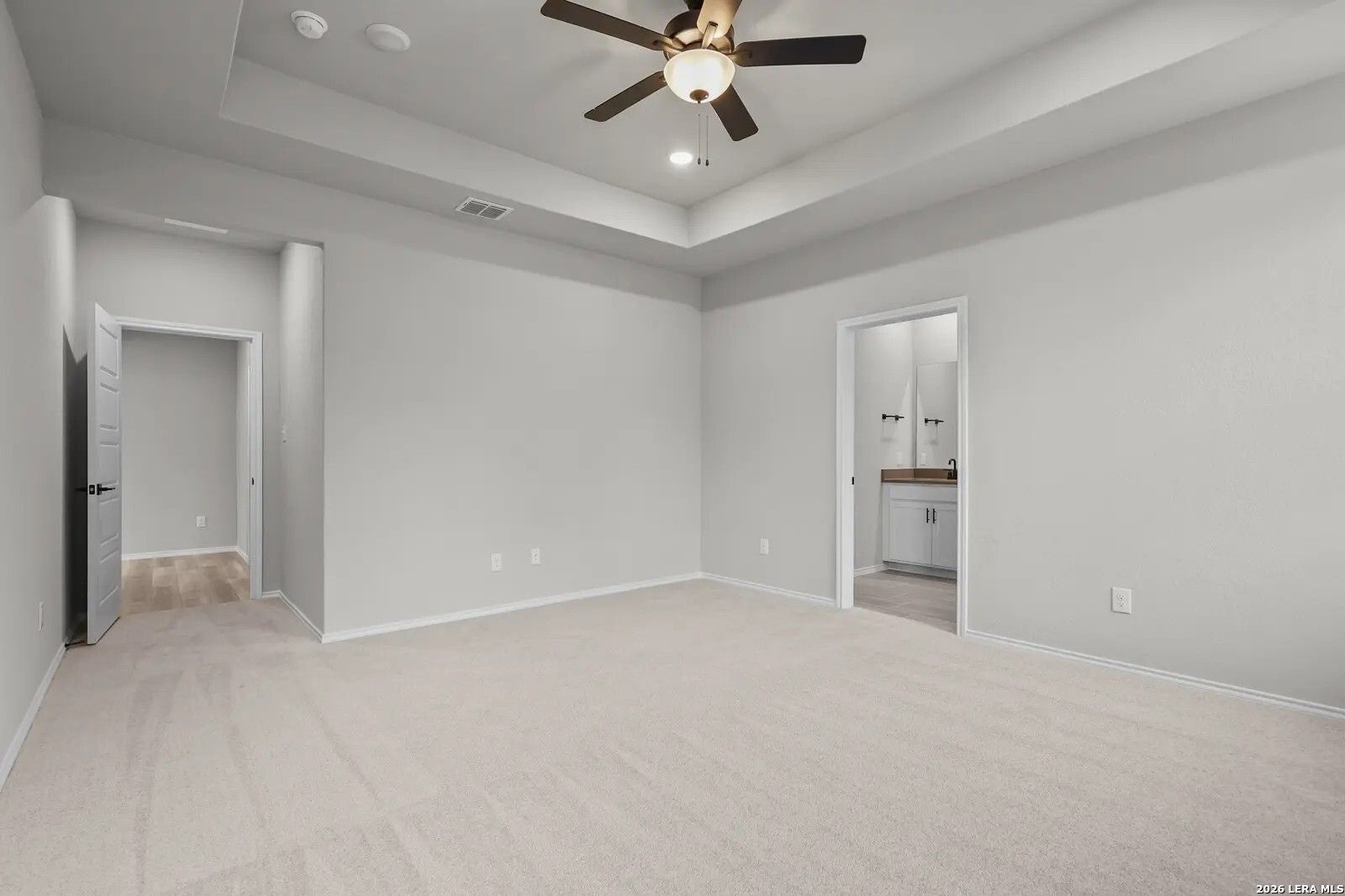Spacious primary bedroom with tray ceiling and ceiling fan in The Glenwood E floor plan at Comanche Ridge, San Antonio.