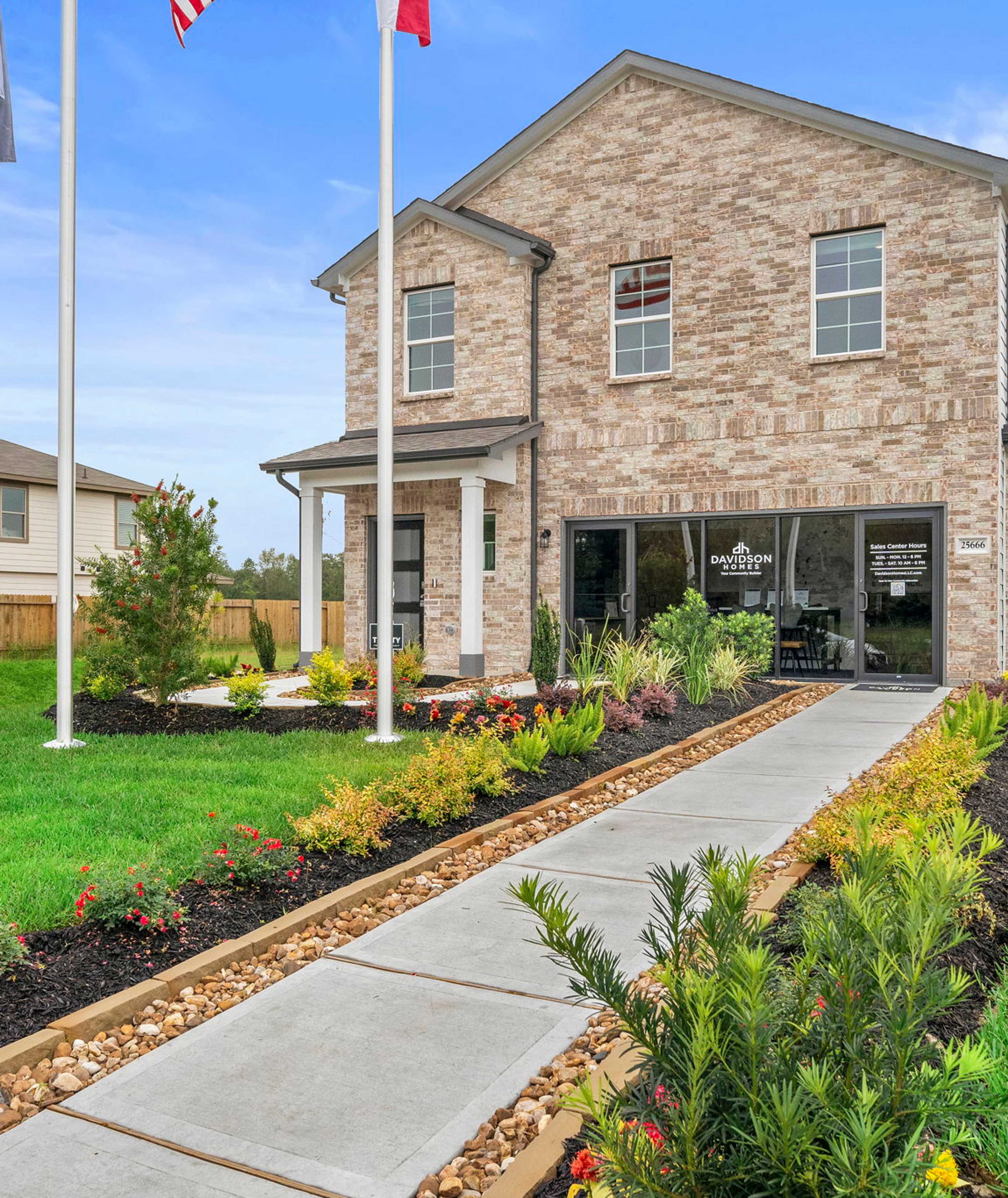 Brick home exterior at Hill & Dale Ranch in Splendora TX with covered porch, flagpoles, flower beds, and stone walkway