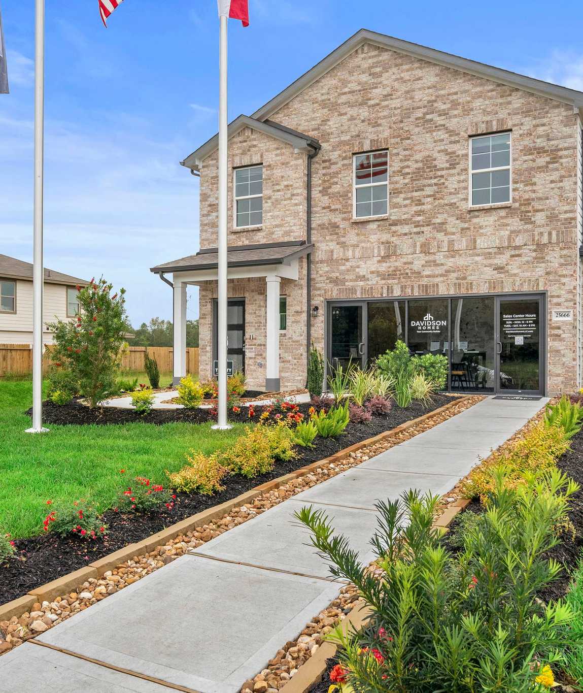 Brick home exterior at Hill & Dale Ranch in Splendora TX with covered porch, flagpoles, flower beds, and stone walkway