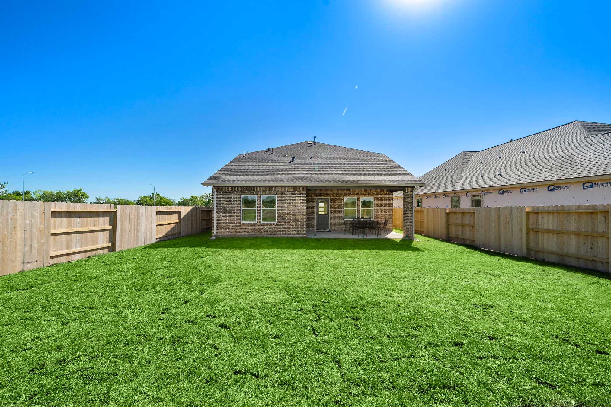 Fenced backyard with lush green lawn, covered patio seating, and single-story home at Emberly in Beasley, Texas