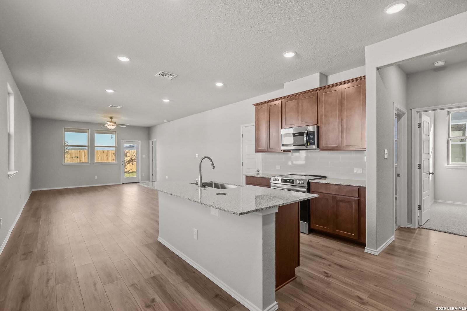 Modern open-concept kitchen with white quartz island, brown shaker cabinets, stainless appliances in The Frio B, San Antonio home