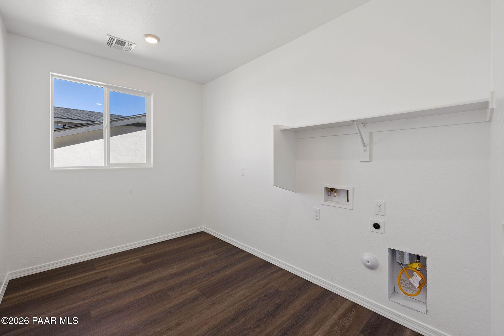 Bright laundry room featuring white walls, large window, recessed shelf, outlets, and plumbing hookups in Davidson Homes The Monarch A, Prescott, AZ