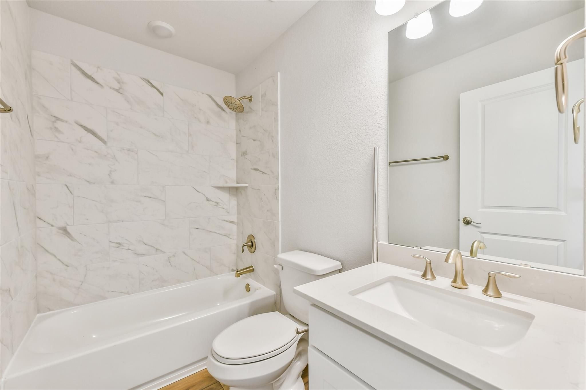 Elegant bathroom featuring marble tile shower, soaking tub, white quartz vanity, and gold fixtures in Davidson Homes The Victoria A, Lago Mar, Texas City
