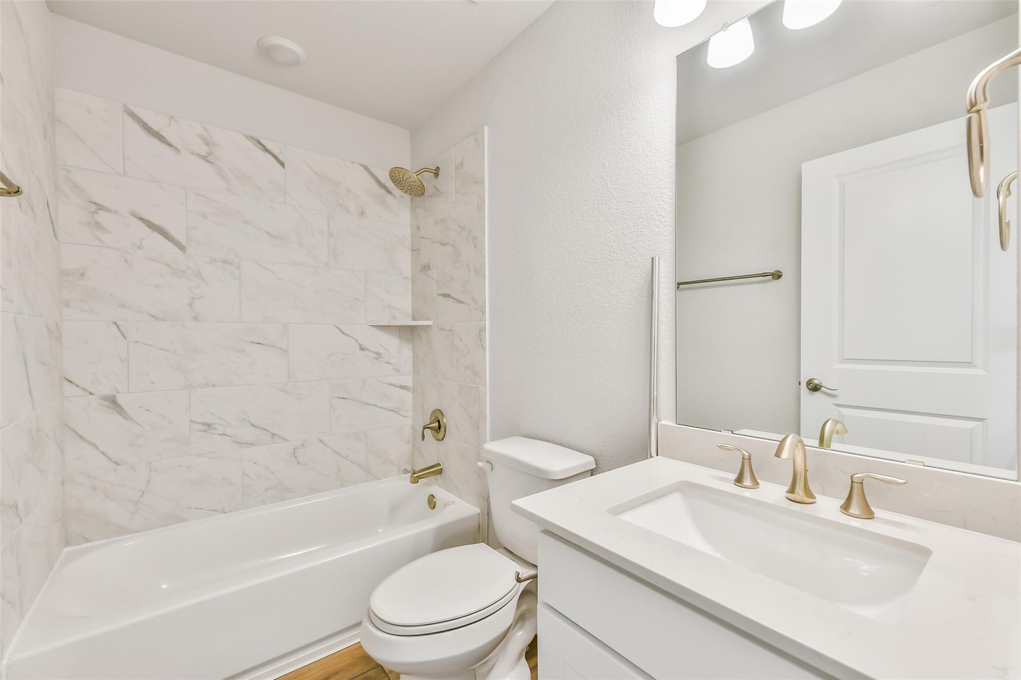 Elegant bathroom featuring marble tile shower, soaking tub, white quartz vanity, and gold fixtures in Davidson Homes The Victoria A, Lago Mar, Texas City