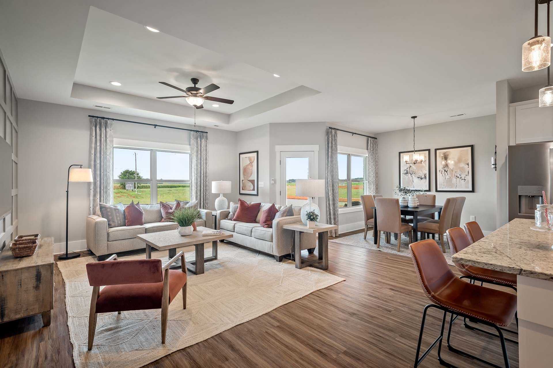 Spacious open-concept living and dining area in Heritage Lakes, New Market AL by Davidson Homes with hardwood floors, large windows, and neutral furnishings