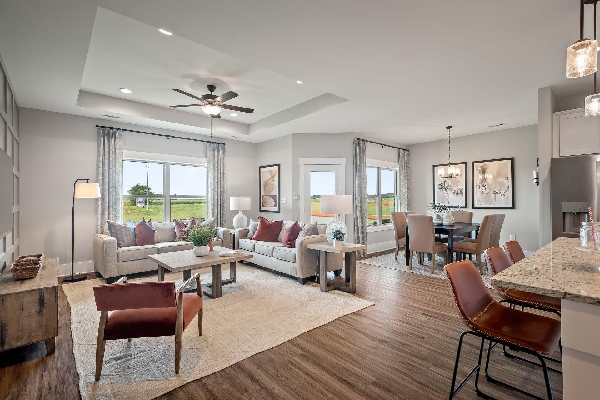 Spacious open-concept living and dining area in Heritage Lakes, New Market AL by Davidson Homes with hardwood floors, large windows, and neutral furnishings