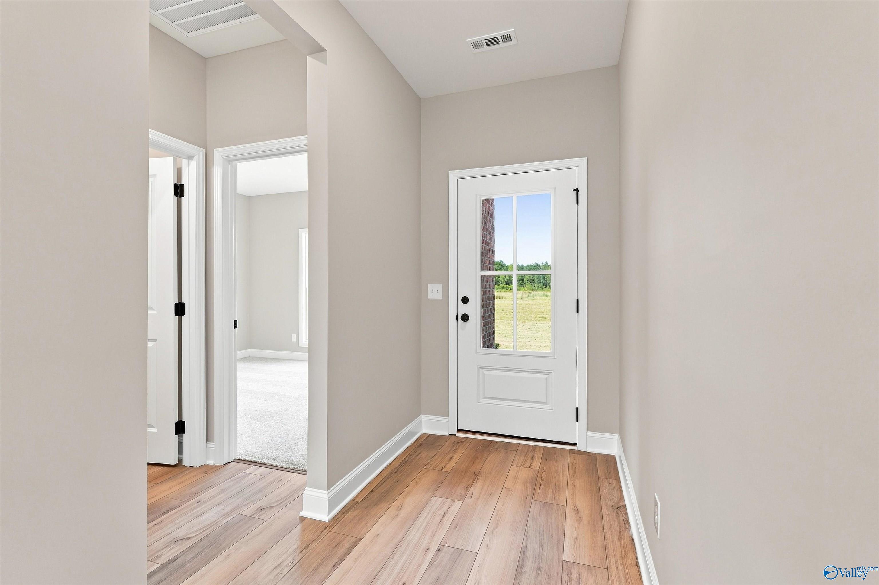 Bright foyer with glass-panel front door, hardwood-style flooring, and neutral walls in Davidson Homes' The Franklin C, Toney, Alabama