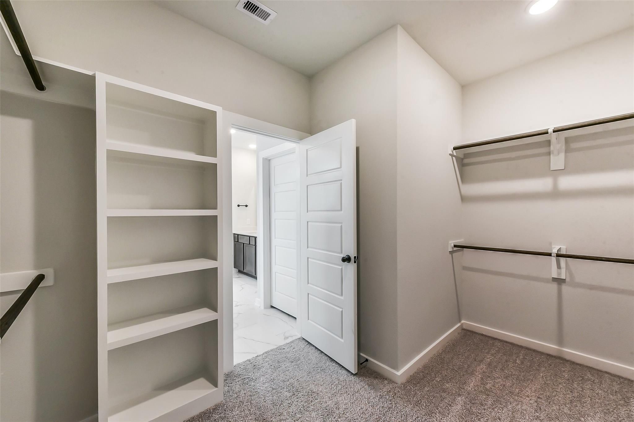 Spacious walk-in closet with white shelving and hanging rods opening to ensuite bathroom in Davidson Homes Sequoia C, Crosby Texas